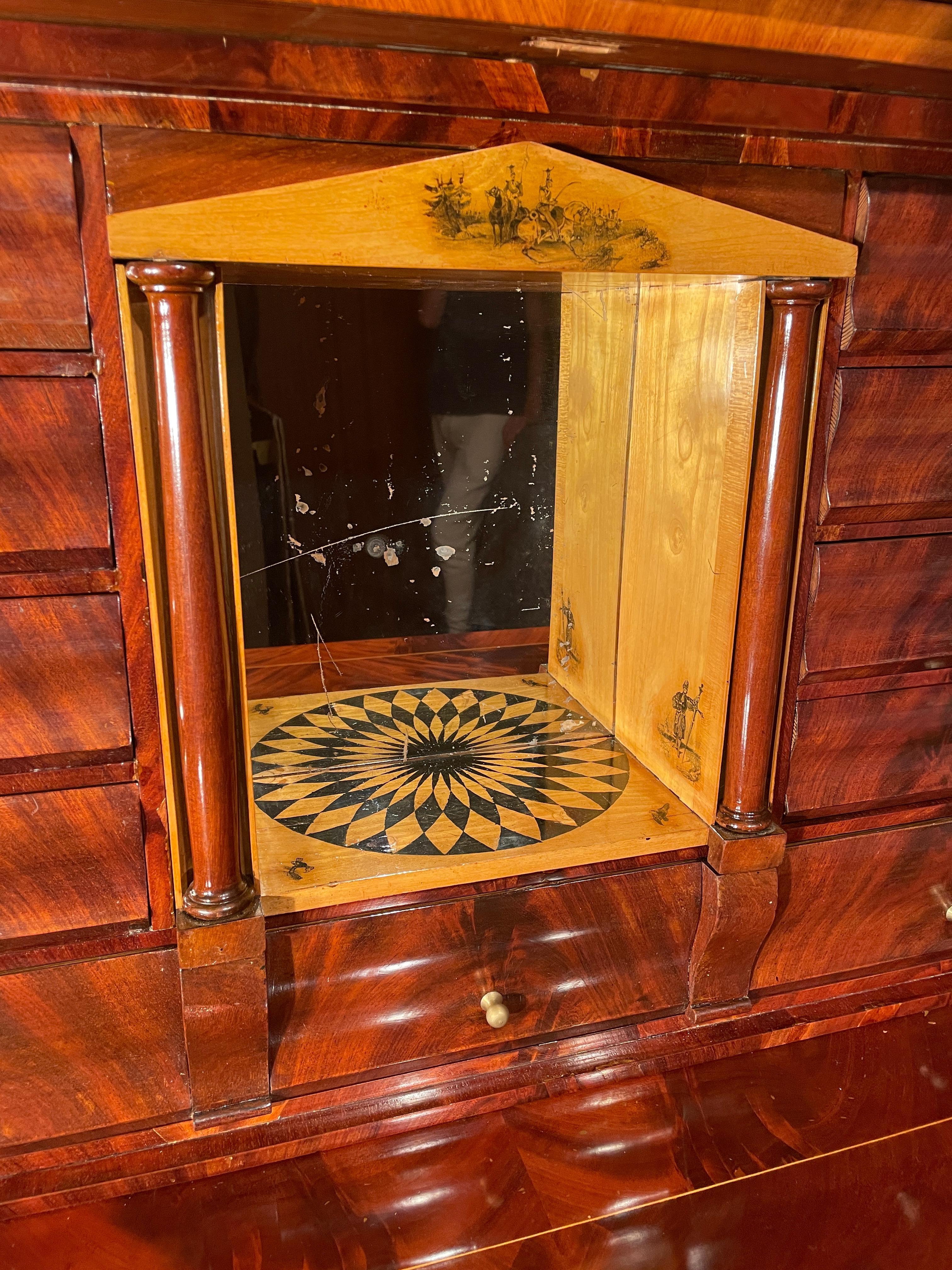 Empire drop front desk, Copenhagen 1810-20.
This unique Danish secretary desk is embellished with mahogany veneer. The lower part has three curved drawers. Two columns frame the writing flap and the lower drawers. The upper part is decorated with