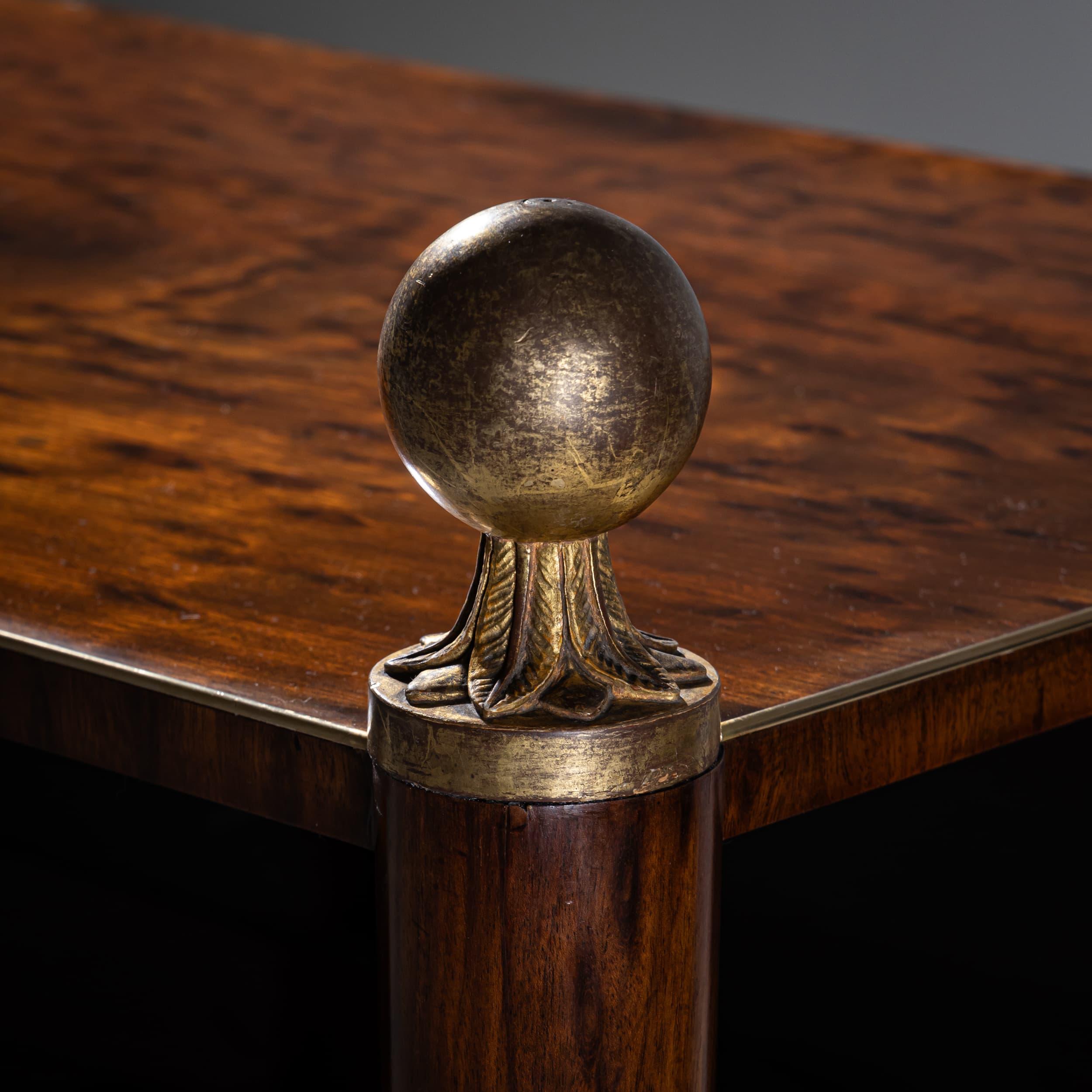 Etagère in stile impero che poggia su gambe affusolate con sabot in ottone patinato e terminali a sfera in legno. Quattro ripiani, delimitati da un delicato profilo in ottone, offrono un elegante spazio di archiviazione. Il pannello posteriore a