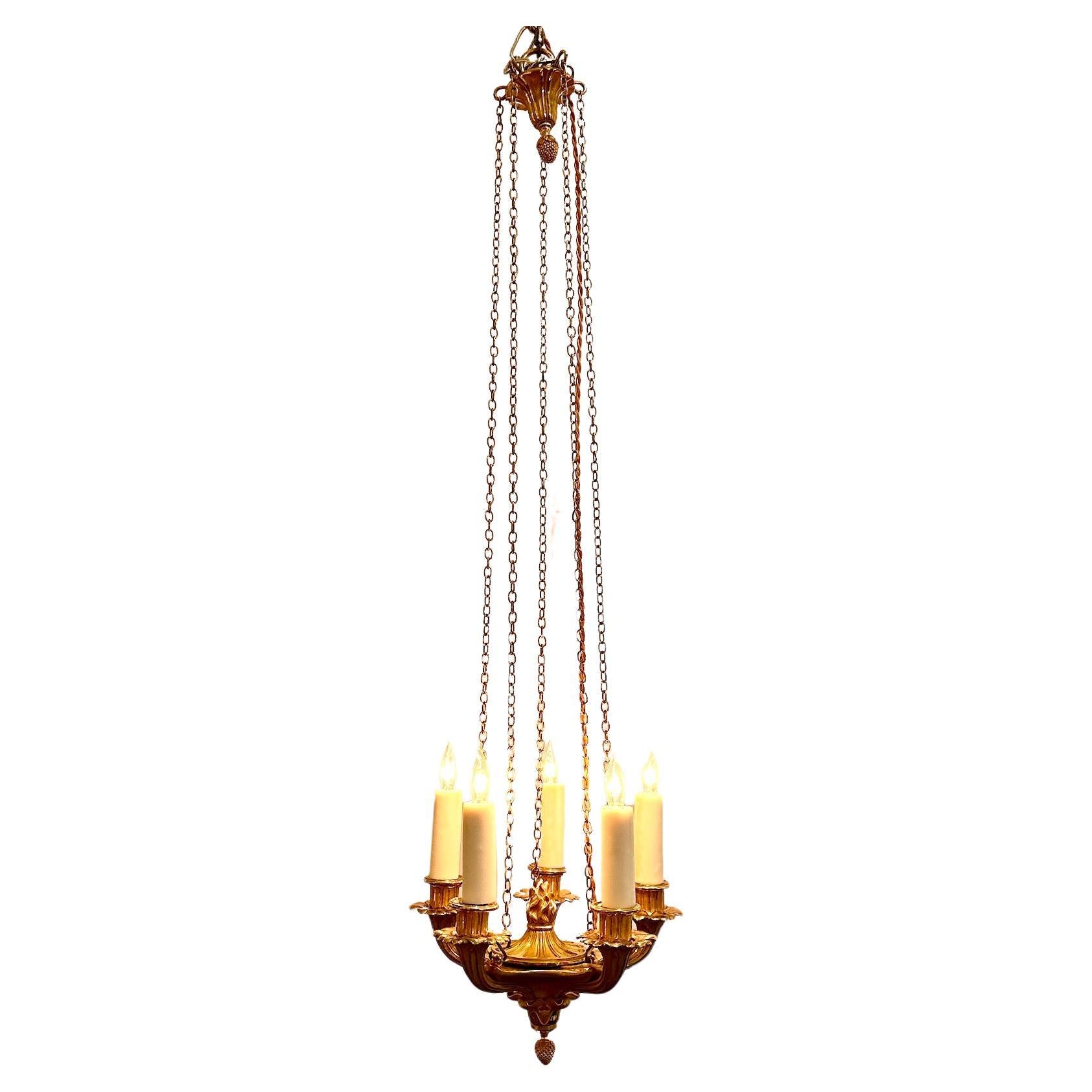 Un affascinante e raffinato lampadario Impero a 5 luci in bronzo dorato con catena e baldacchino.  Manicotti per candele di cera bianco sporco da 3,5