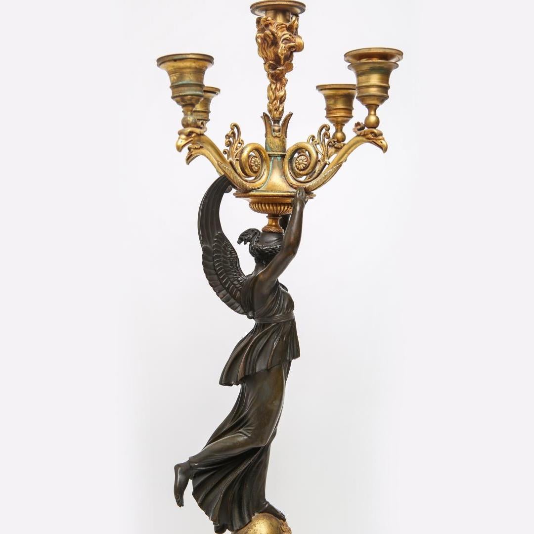 Fine quality pair of patinated and gilt bronze Empire candelabras; the central atop a flame support and the surrounding four on Napoleonic eagle-head arms, all above a figural caryatid column depicting Nike or Winged Victory, her foot upon an orb
