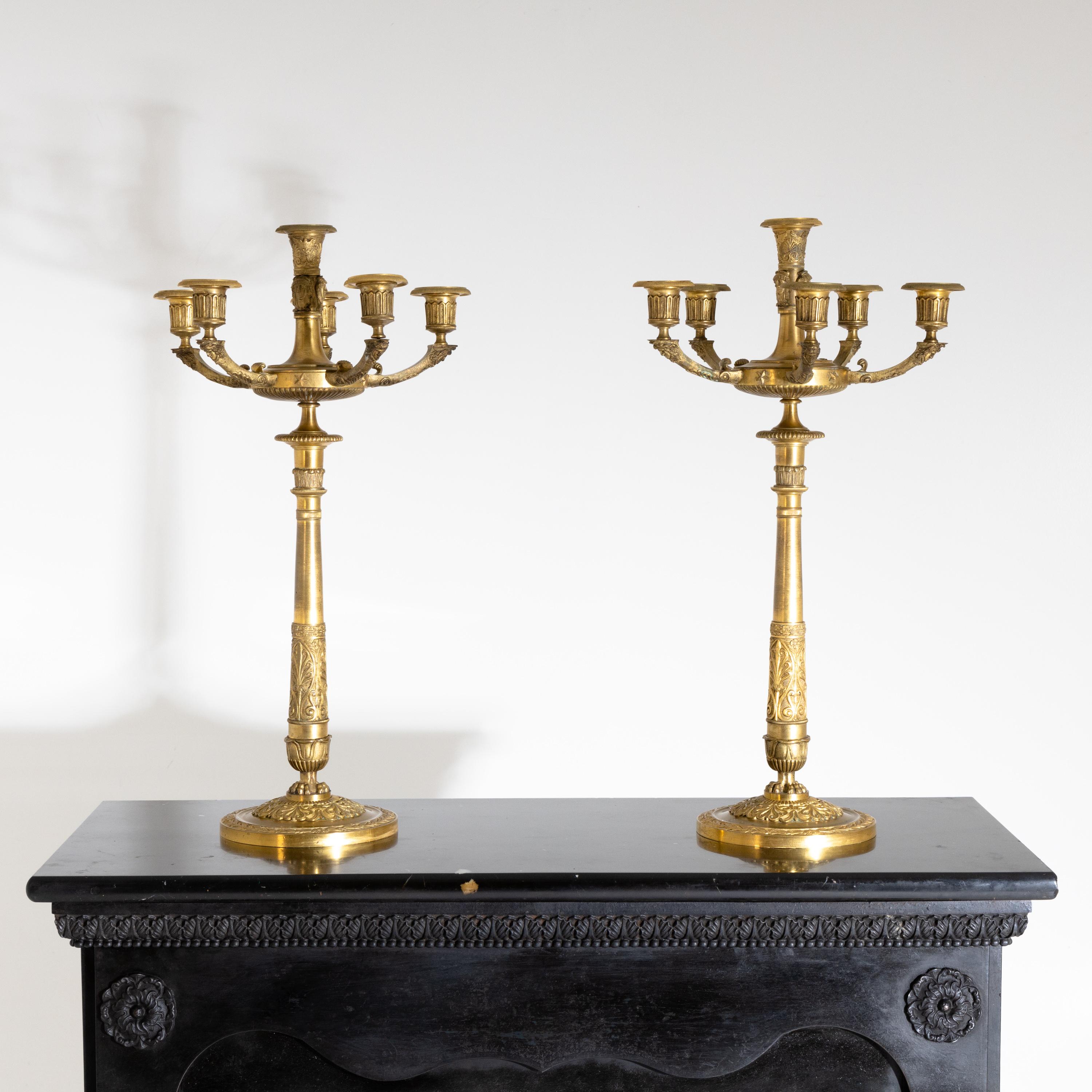 Pair of Empire girandoles of fire-gilt bronze, on a round base with acanthus leaf decoration and six spouts. The candelabra arms and central spout are decorated with mascarons and tendrils.