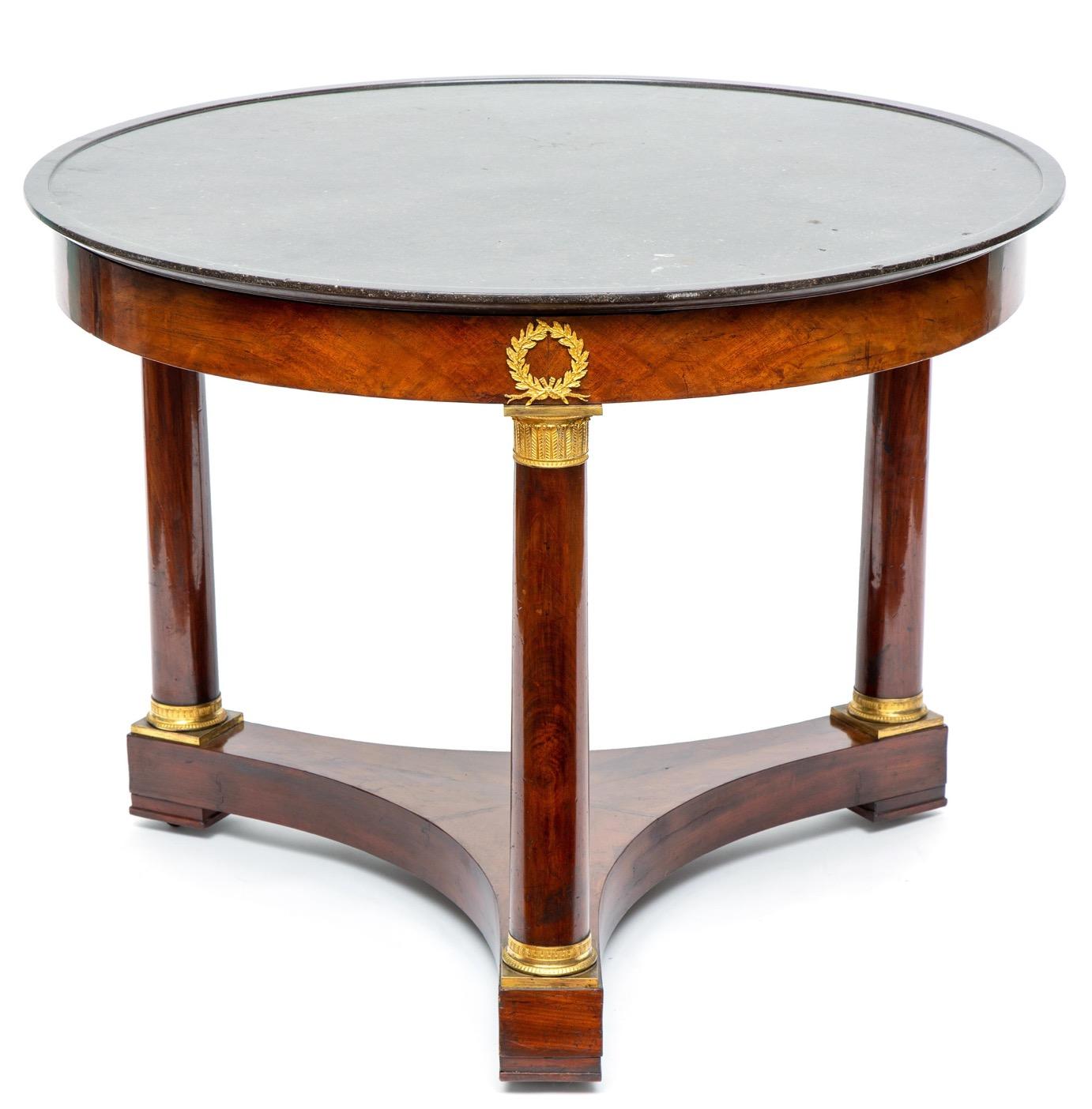 A very nice mahogany empire gueridon or center table with gilt bronze mounts and a black marble top. The marble top sculptured with a raised outer rim. The top frame is hold up by three gilt bronze mounted mahogany columns that rest on a tripod