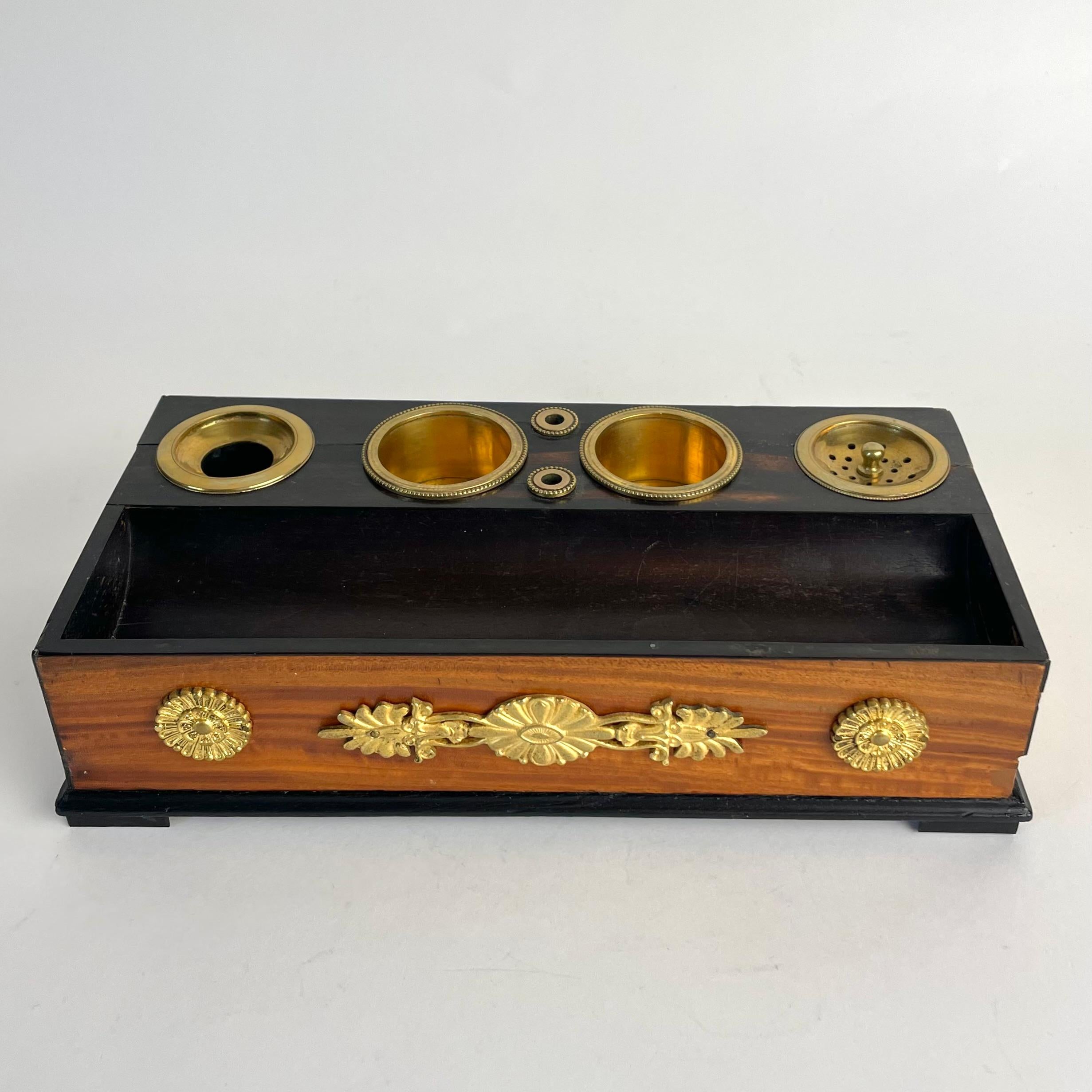 
Calamaio Impero in mogano e noce ebanizzato con montature in bronzo dorato, 1820 ca.

Un calamaio Impero raro e finemente lavorato, risalente agli anni venti del XIX secolo. Realizzato in mogano a grana fine (probabilmente sapele) con elementi in