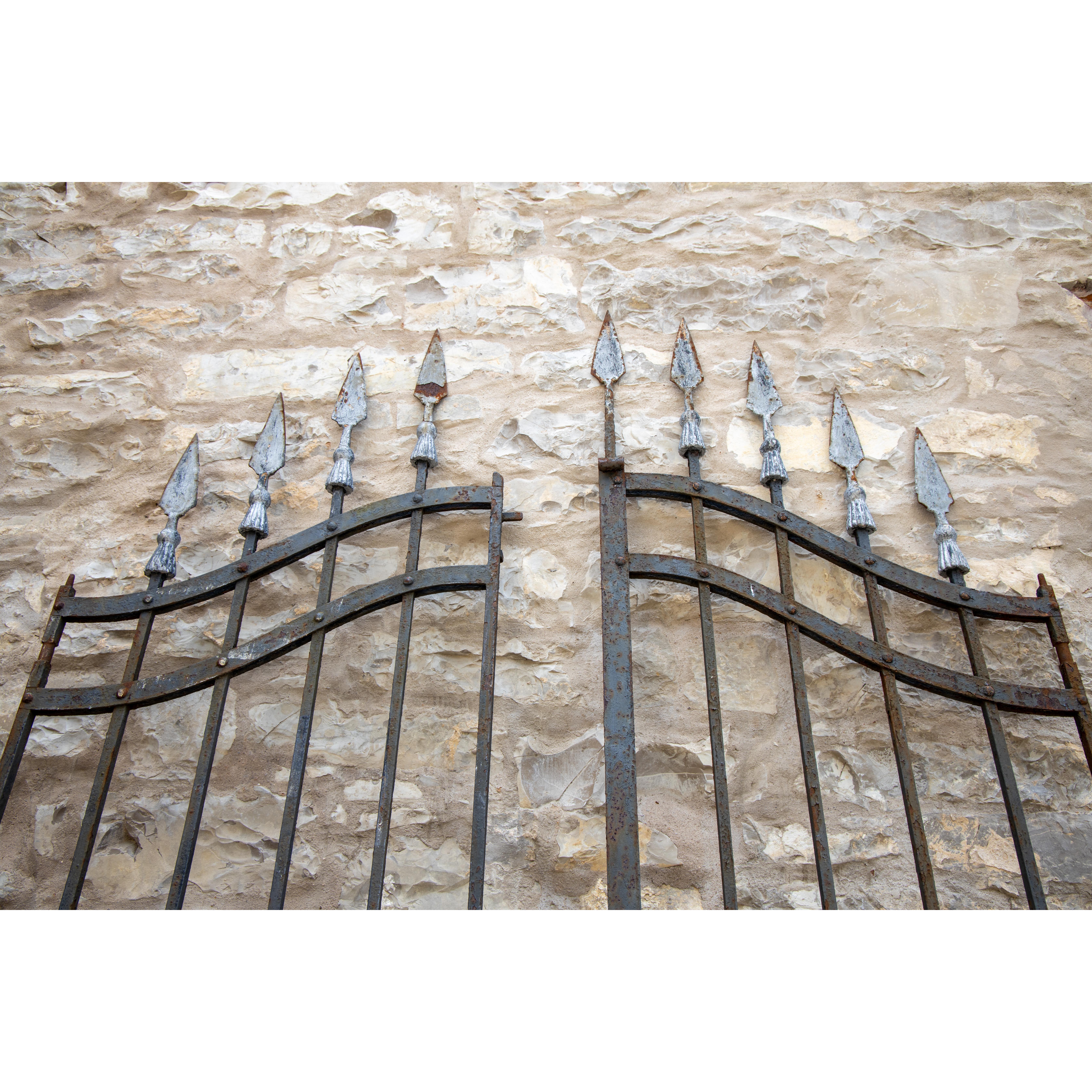 Large wrought iron court gate with two wings and an arched top with silver-patinated arrowheads.