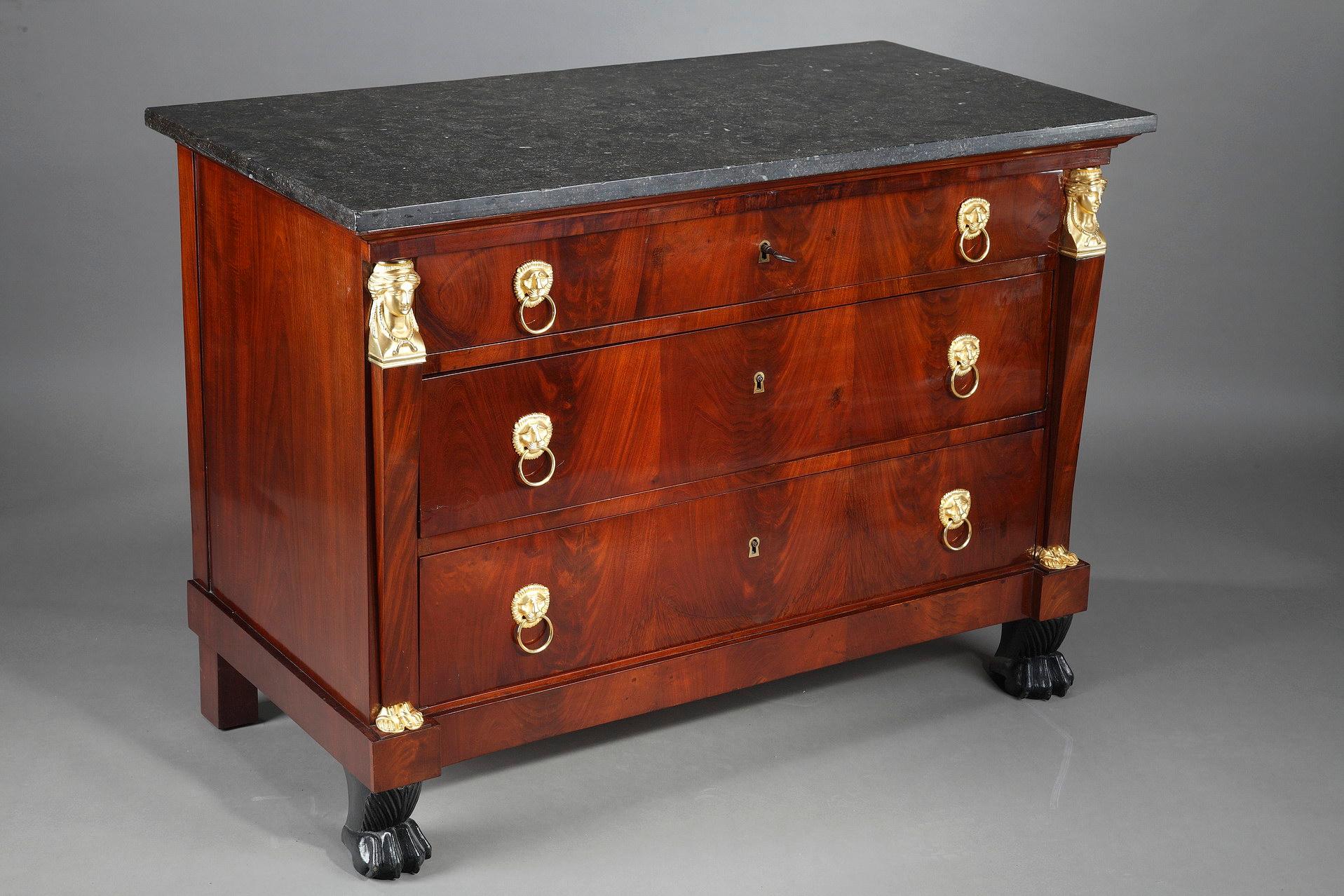Empire mahogany and mahogany veneer commode opening with three drawers adorned with drop handles in the form of bullheads. On either side of the commode, the pilaster are decorated with busts of Athenians and chased gilt bronze feet, and rest on