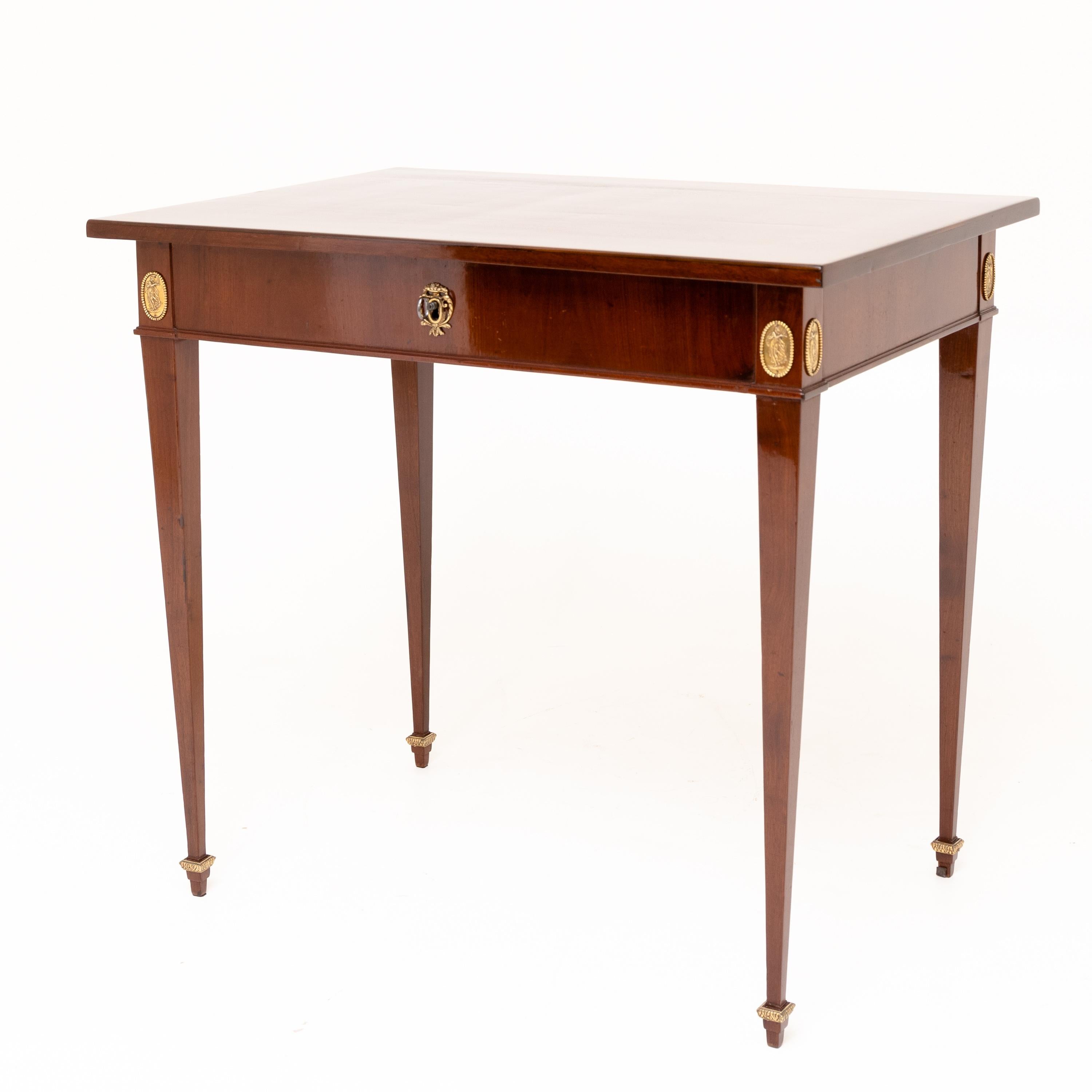 Mahogany table standing on four tall slender and square legs with slightly cranked corners with medallion decoration and rectangular tabletop. The tabletop can be pushed back and reveals the lockable compartment hidden in the frame.