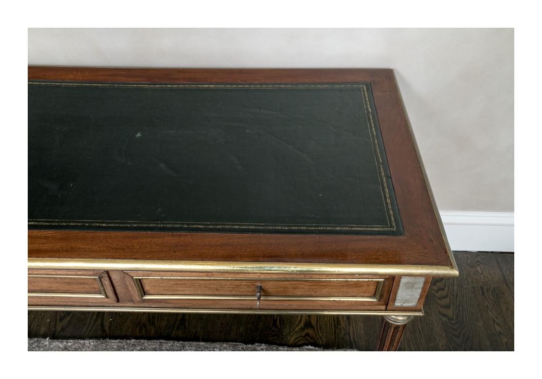 Empire mahogany desk with tooled hunter green leather top. The desk with bronze banding and trim, bronze finely fluted corner medallions, fluted and tapering legs with bronze caps and mounts. The desk is paneled all around with bronze trim. Lacking