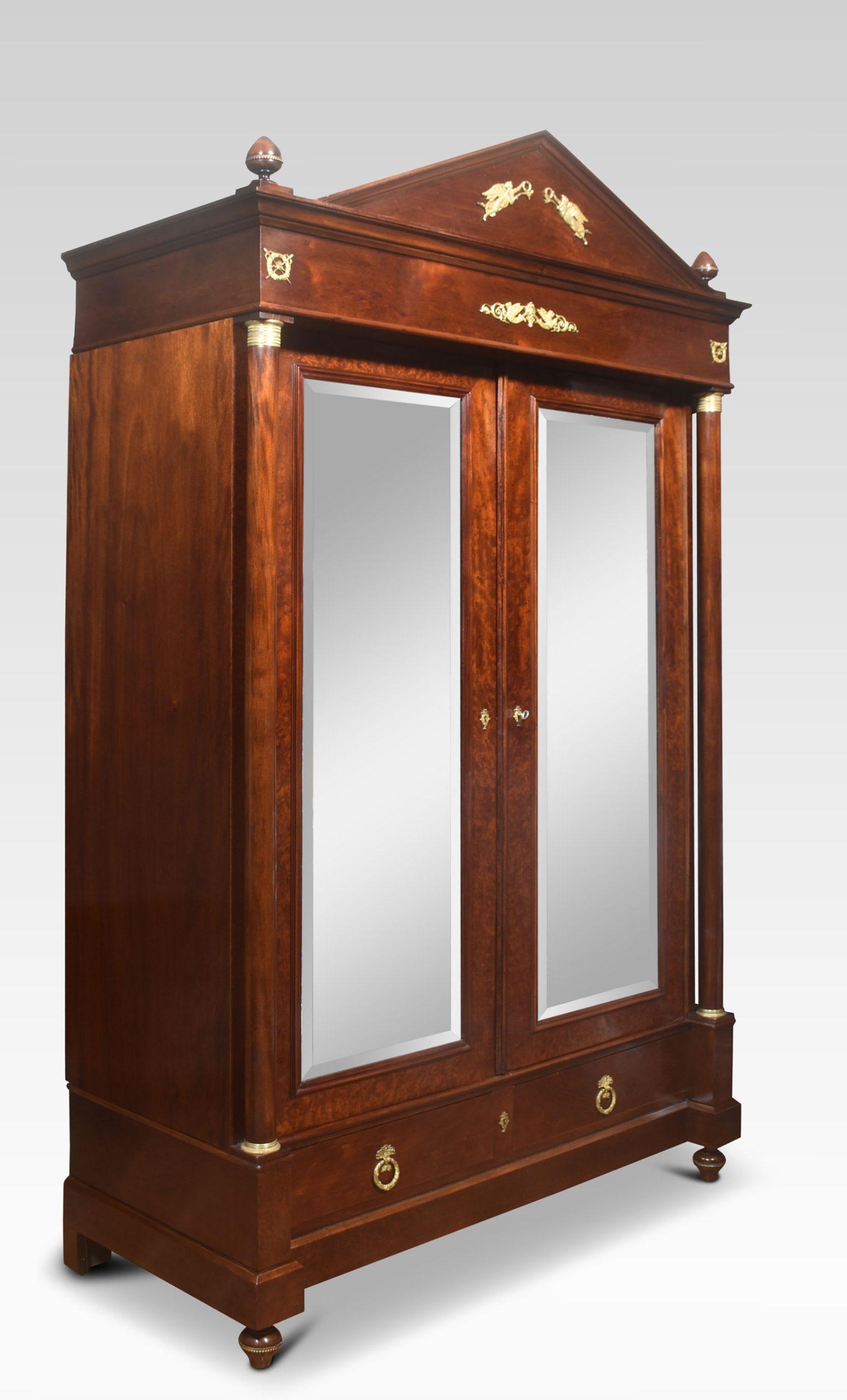 Empire wardrobe, the projecting removable cornice with brass decoration flanked by turned finials. Above two large beeveled mirror doors opening to reveal large hanging area. FLanked by circular colums with brass capitals. To the base section fitted
