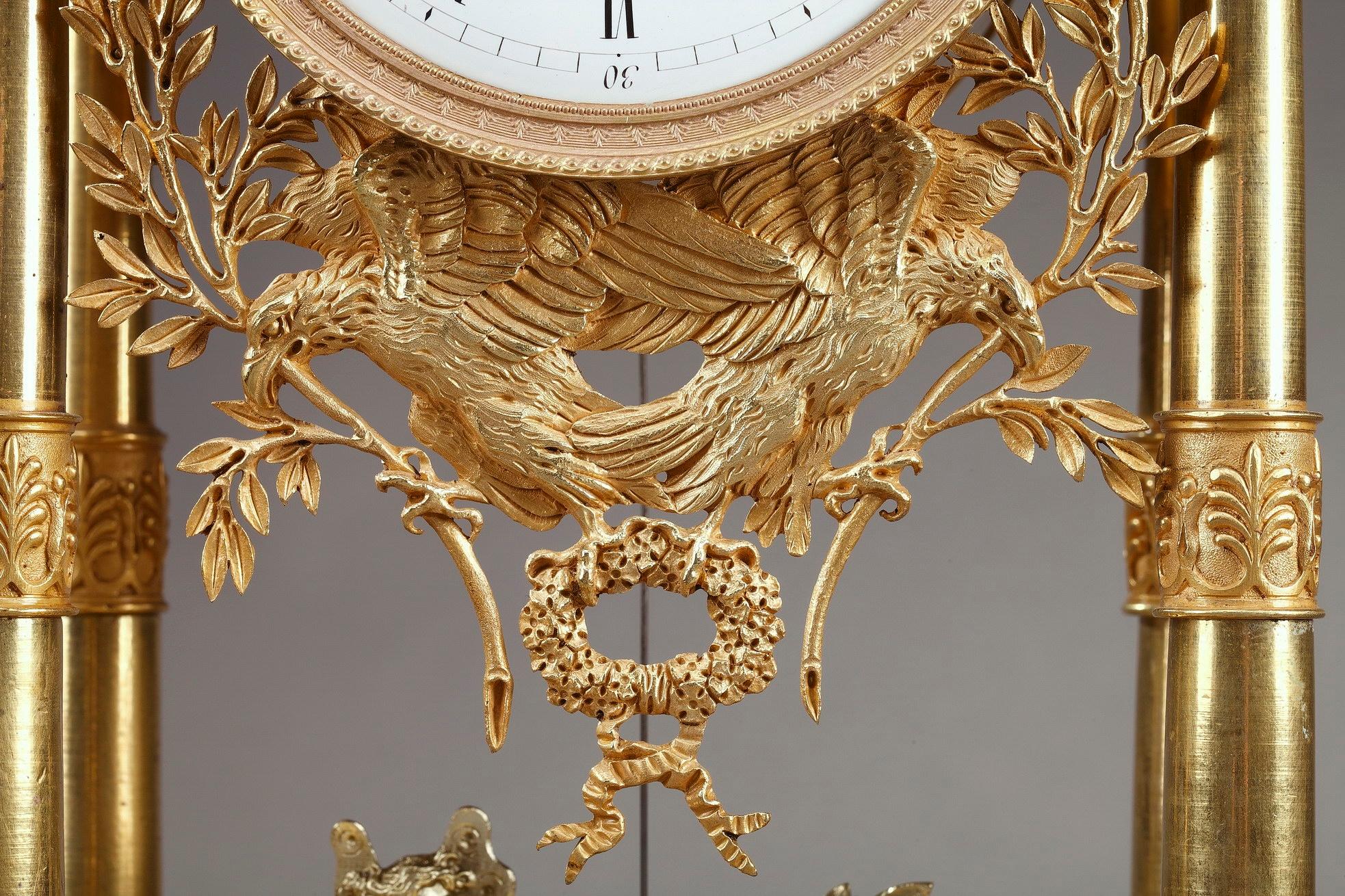 Empire mantel clock in ormolu, or gilt bronze, designed as a portico, with four columns decorated with foliage and palmette. The columns support the entablature embellished with Pegasus and topped by a putto sculpting an antique bust. The dial with