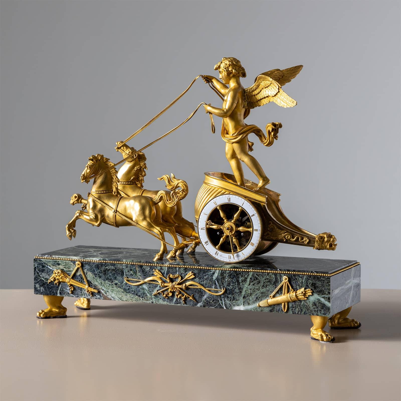 French mantel clock crafted from fire-gilt bronze, featuring a green marble plinth supported by paw feet. Atop the clock sits Cupid, depicted as a charioteer riding a two-horse chariot with dynamic motion. The clockwork is housed within the chariot,