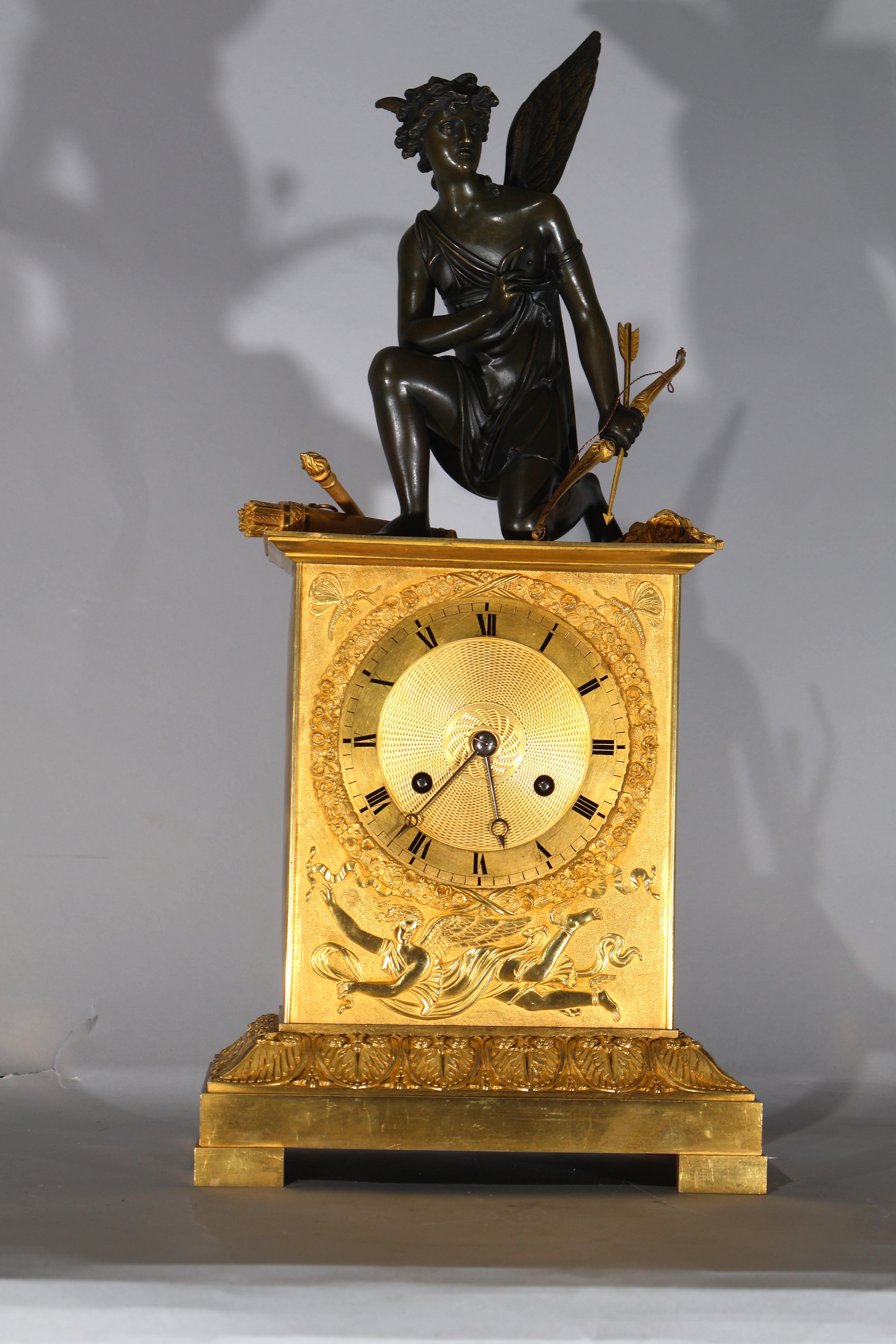 An Exquisite Period Empire Clock, featuring Cupid (in patinated bronze) with his bow & arrow, next to him a quiver & torch. The body of the clock with bas relier decoration and anthemia. Silk thread suspension, pendulum & key. France, circa 1800.