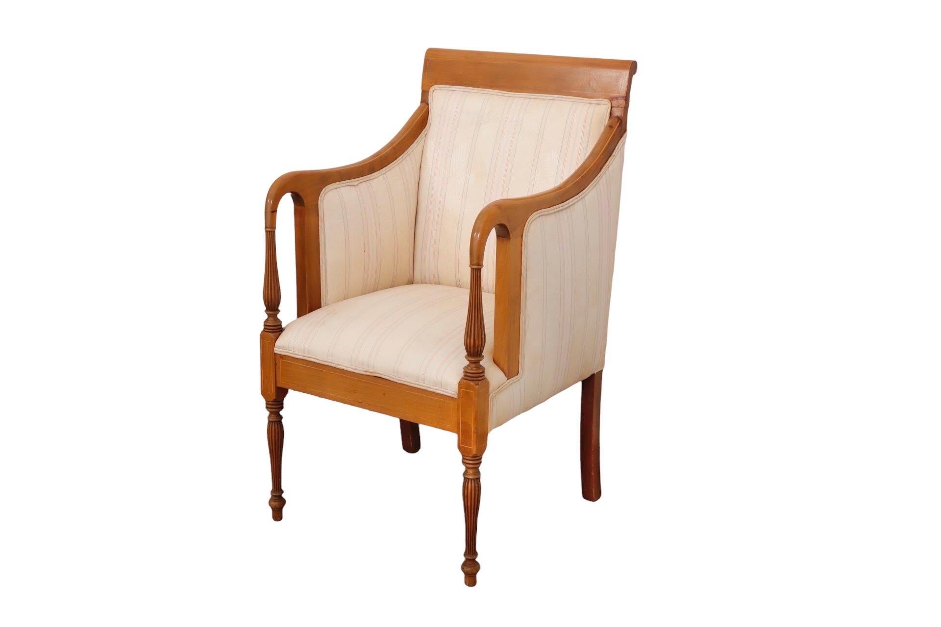 Empire style armchair made of maple. A flat crest rail and downswept reeded arms are both inlaid with blond maple. Front legs are turned and reeded finished with turnip feet. The front back, seat and back are upholstered with vintage striped beige