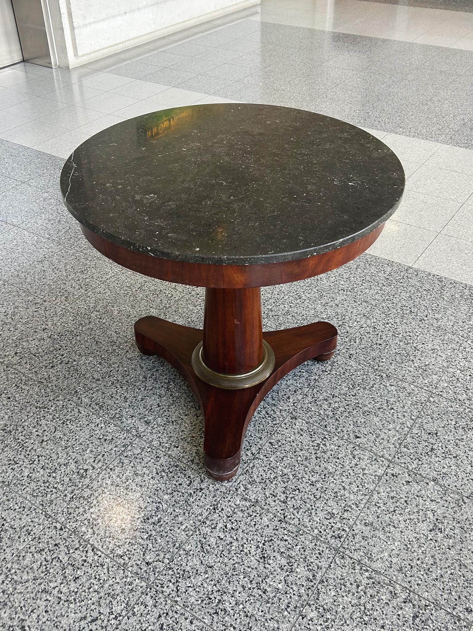 Esta mesa redonda Imperio francés del siglo XIX consta de un tablero de mármol negro y una base de pedestal de caoba. La caoba bronceada tiene un rico tono marrón rojizo, mientras que el mármol presenta motas de grises. Una mesa sutilmente decorada