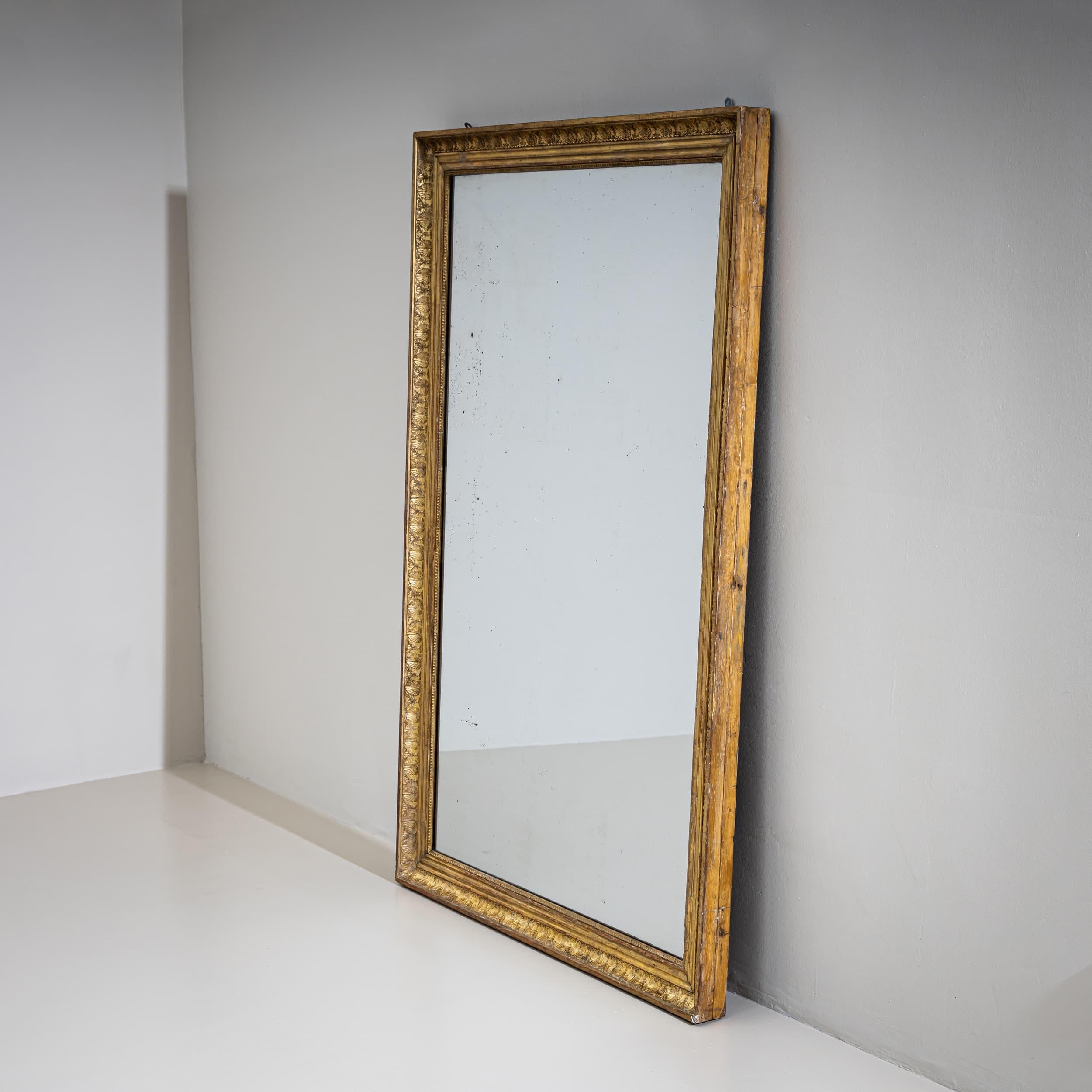 Gran espejo de pared de estilo Imperio Neoclásico, hacia 1810. El marco rectangular está dorado y adornado con ornamentos de estuco aplicados, que incluyen hojas de acanto estilizadas y cálices de hojas. El cristal del espejo antiguo presenta