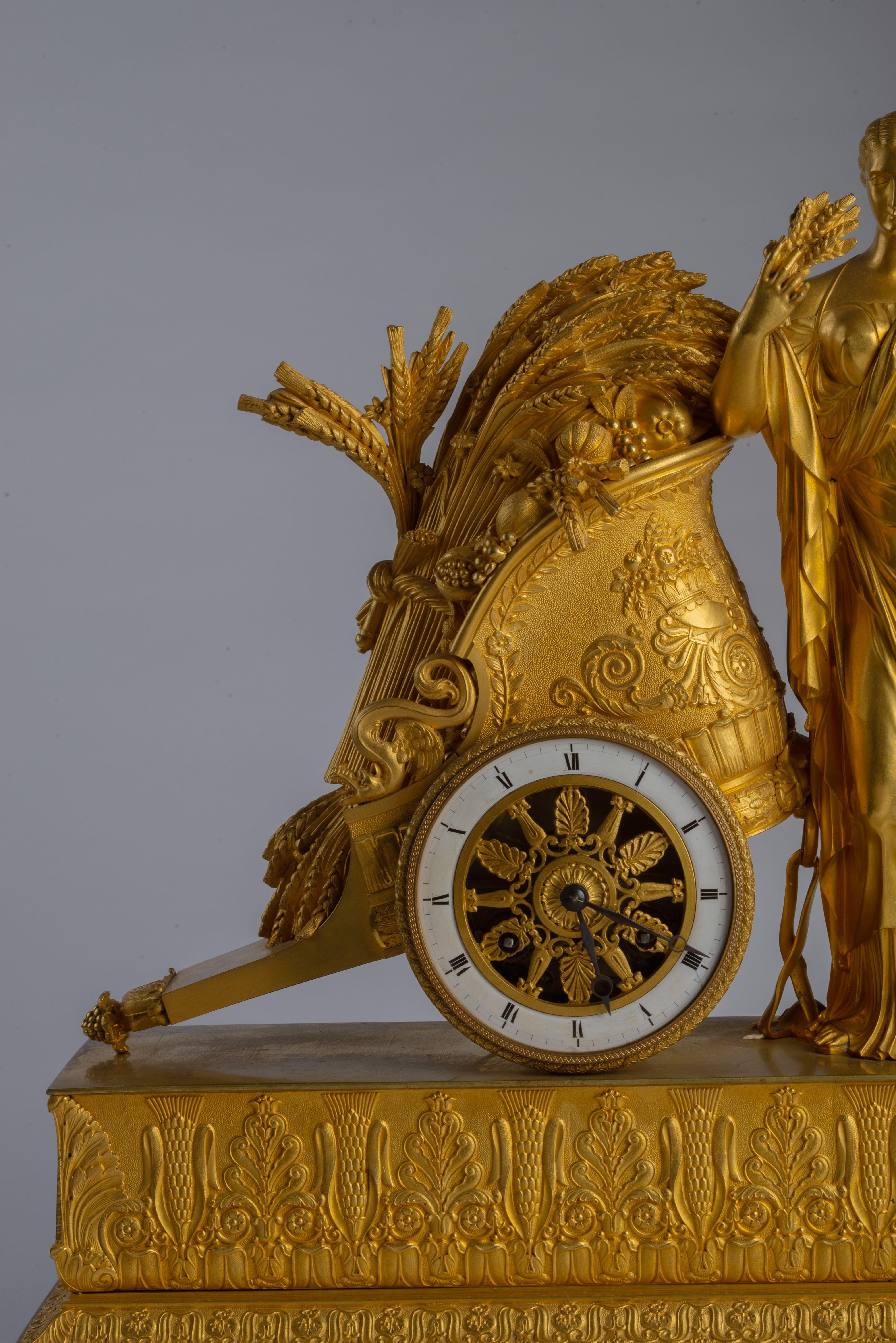 The rectangular base decorated with a wheat and foliate frieze and raised on four ball feet, the goddess of agriculture Ceres standing while leaning against a Roman chariot with harvested wheat, the dial with roman numerals forming its wheel.
The