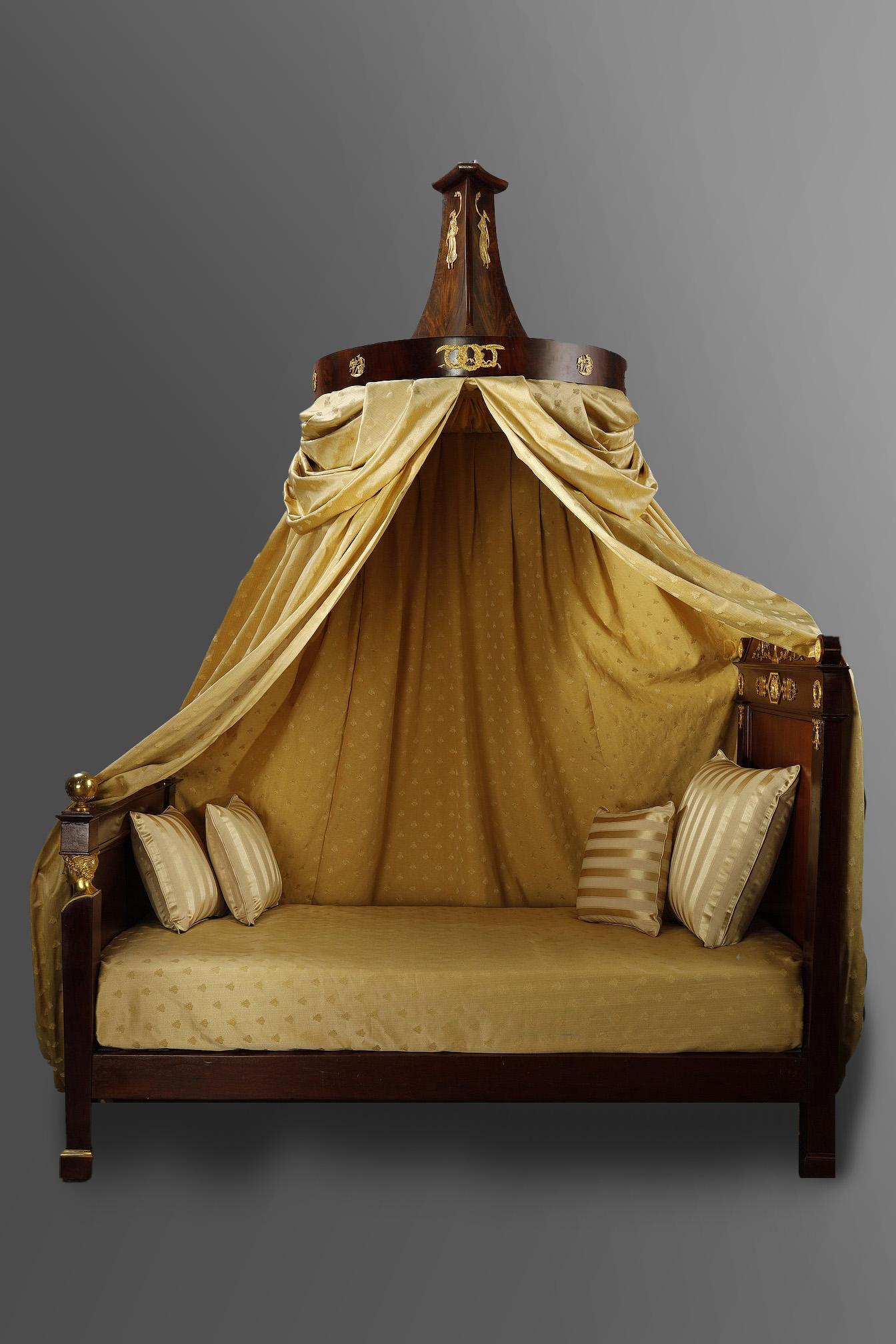 Empire period bed in solid mahogany and mahogany veneer, richly decorated with finely chased and gilded bronzes, with its canopy. The front of the bed features a lyre in the center, framed by two sheath feet with shafts decorated with caduceus and
