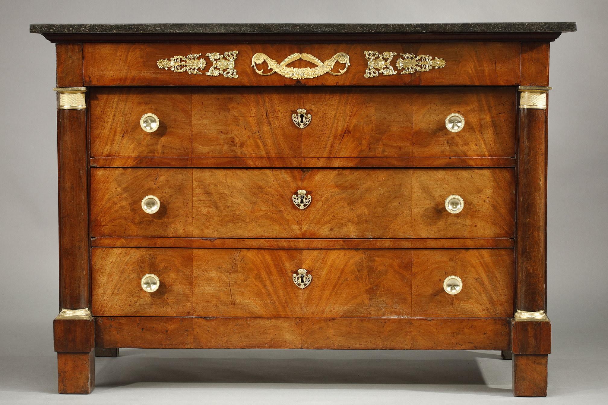 Chest of drawers in flamed mahogany veneer from the Empire period. It is composed of a drawer in the belt and three drawers in the front. The uprights are in the form of straight pillars with gilded capitals and bases. The piece of furniture is