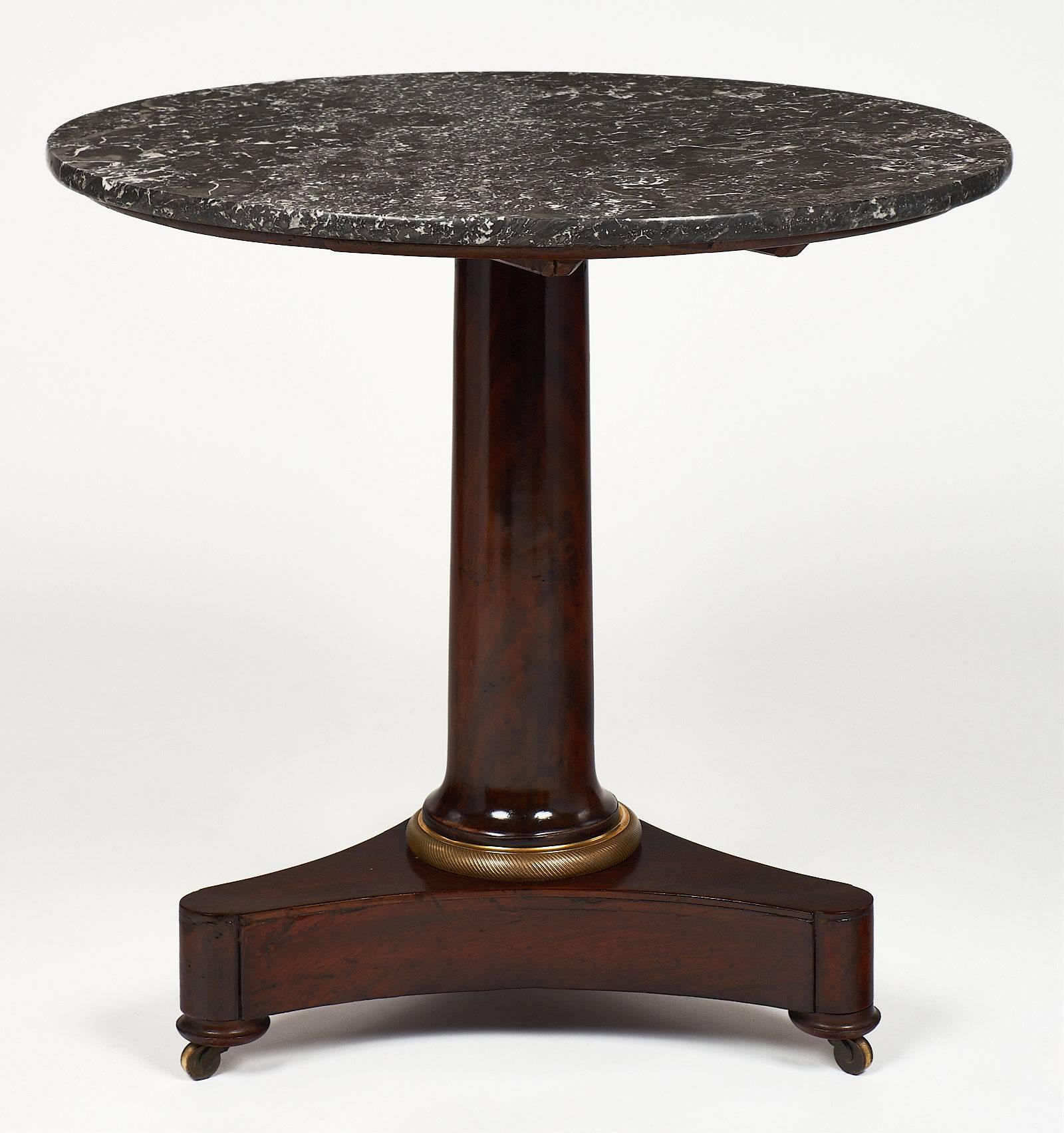 French Empire period gueridon with a gray marble top and a mahogany base. The tripod feet are on casters with a finely cast bronze ring on the center column leg. It is the original Saint Anne marble top.