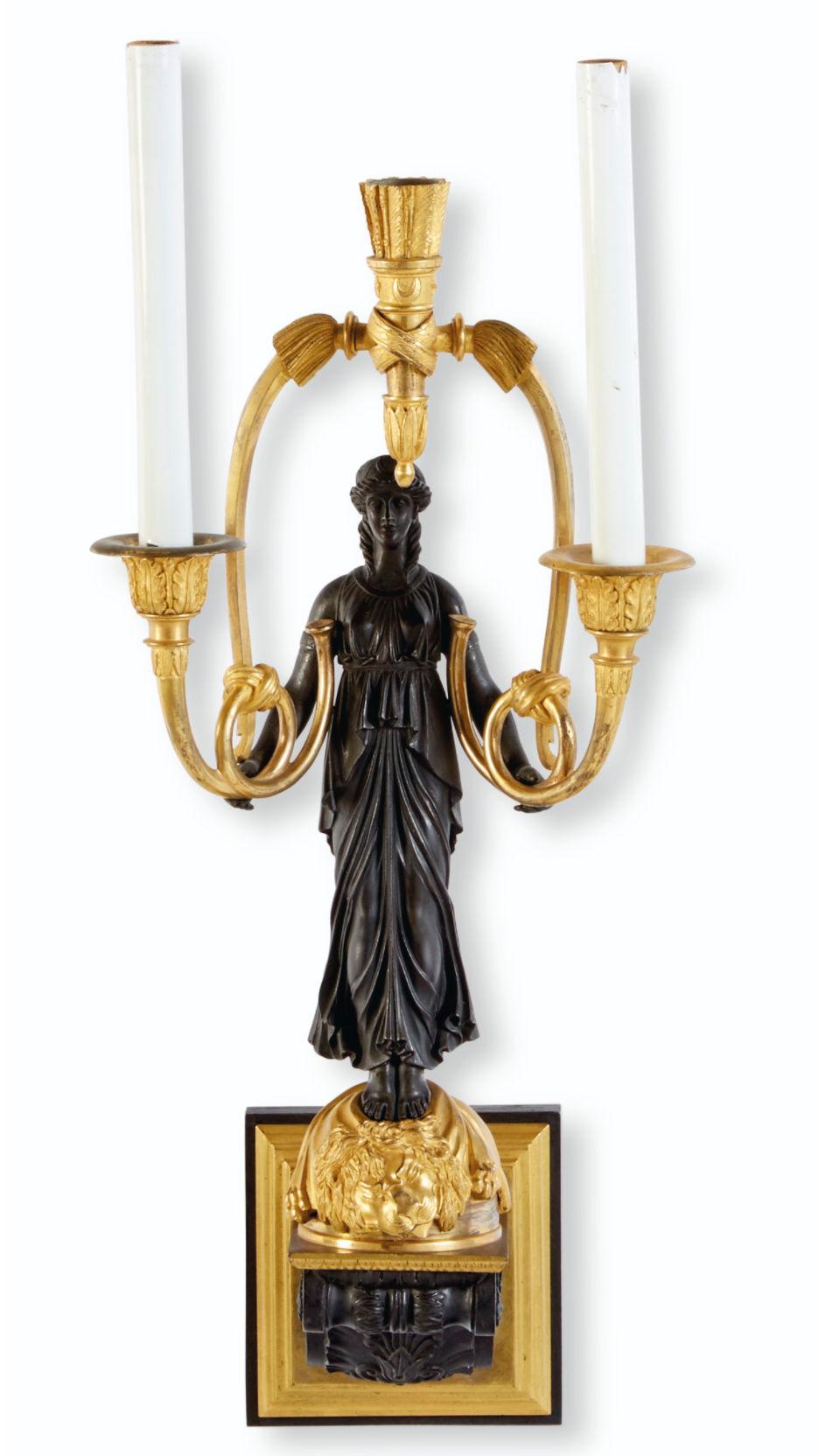 Our exceptional pair of gilt bronze Empire period sconces, circa 1810, feature the patinated figures of neoclassical females holding two candle arms with drapery motif, standing upon round pedestals decorated with a lion's pelt, set upon corbels