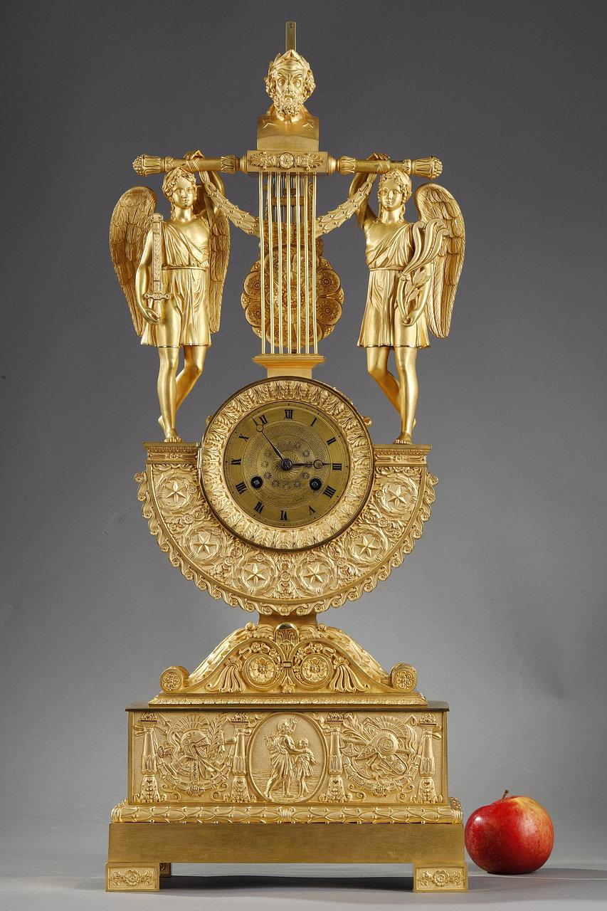 Importante horloge-régulateur entièrement réalisée en bronze doré de la période Empire. Elle a une forme de lyre à sept cordes et un buste d'Homer couronné de lauriers. La façade de l'horloge en bronze doré est décorée dans sa partie inférieure