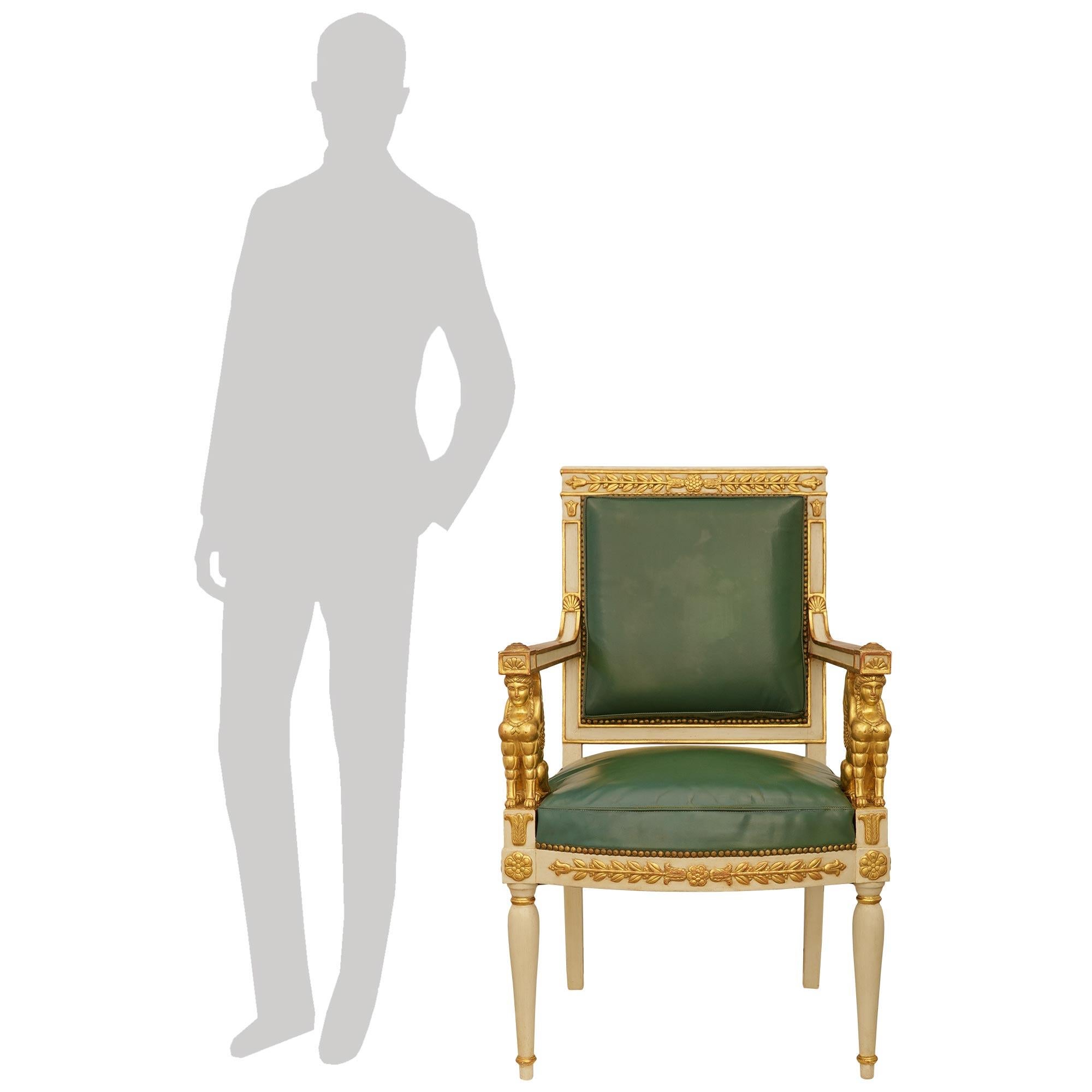 A handsome and most decorative pair of French early 19th century Empire Period patinated Wood and Giltwood armchairs. Each wonderful armchair are raised by two front circular tapered baluster shaped off white patinated legs with top and bottom