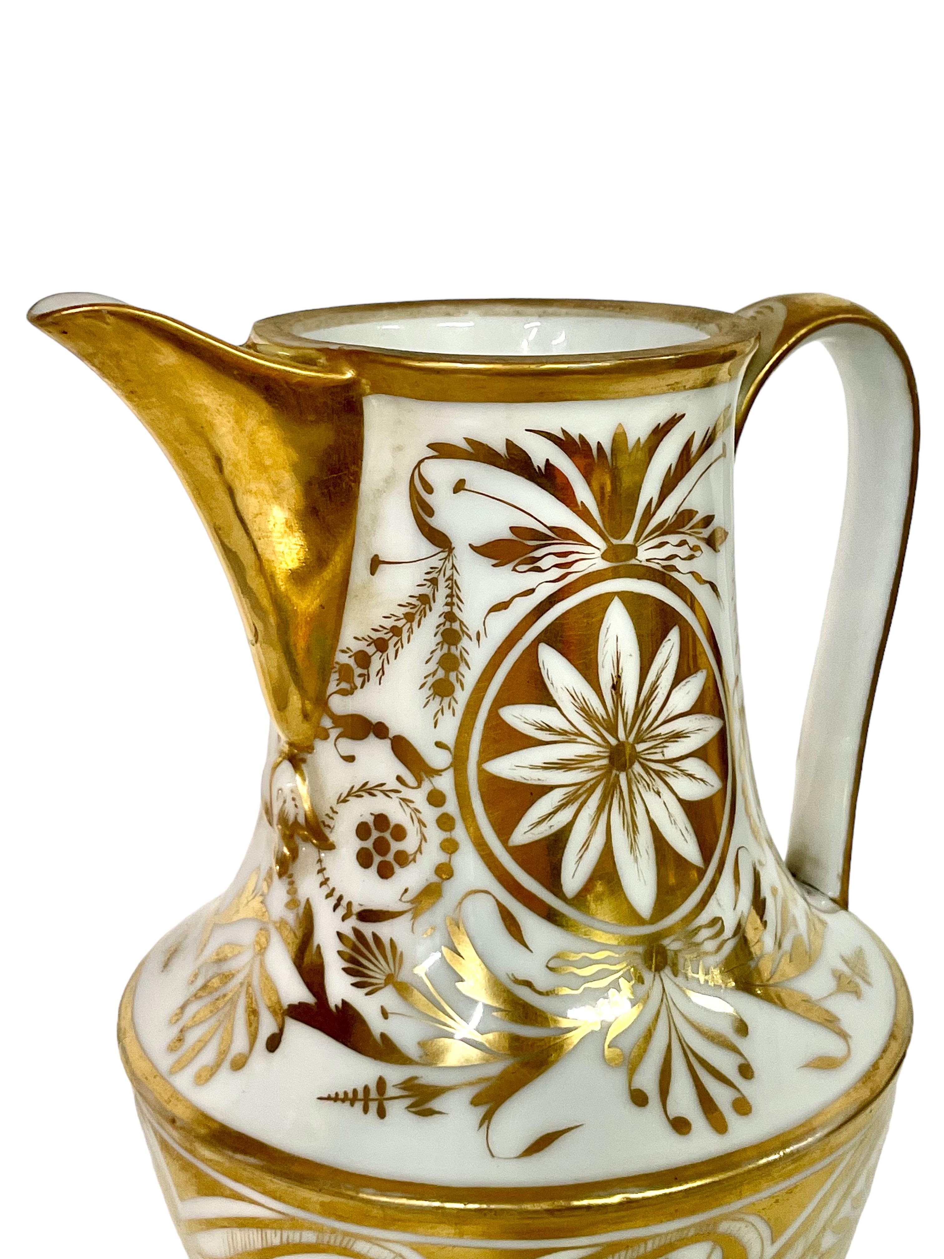 A superb early 19th century Empire period water pitcher in Porcelain de Paris and finely embellished with gilt in a striking, hand-painted design of flowers, leaves and other decorative motifs typical of the period. The upper rim, spout and handle