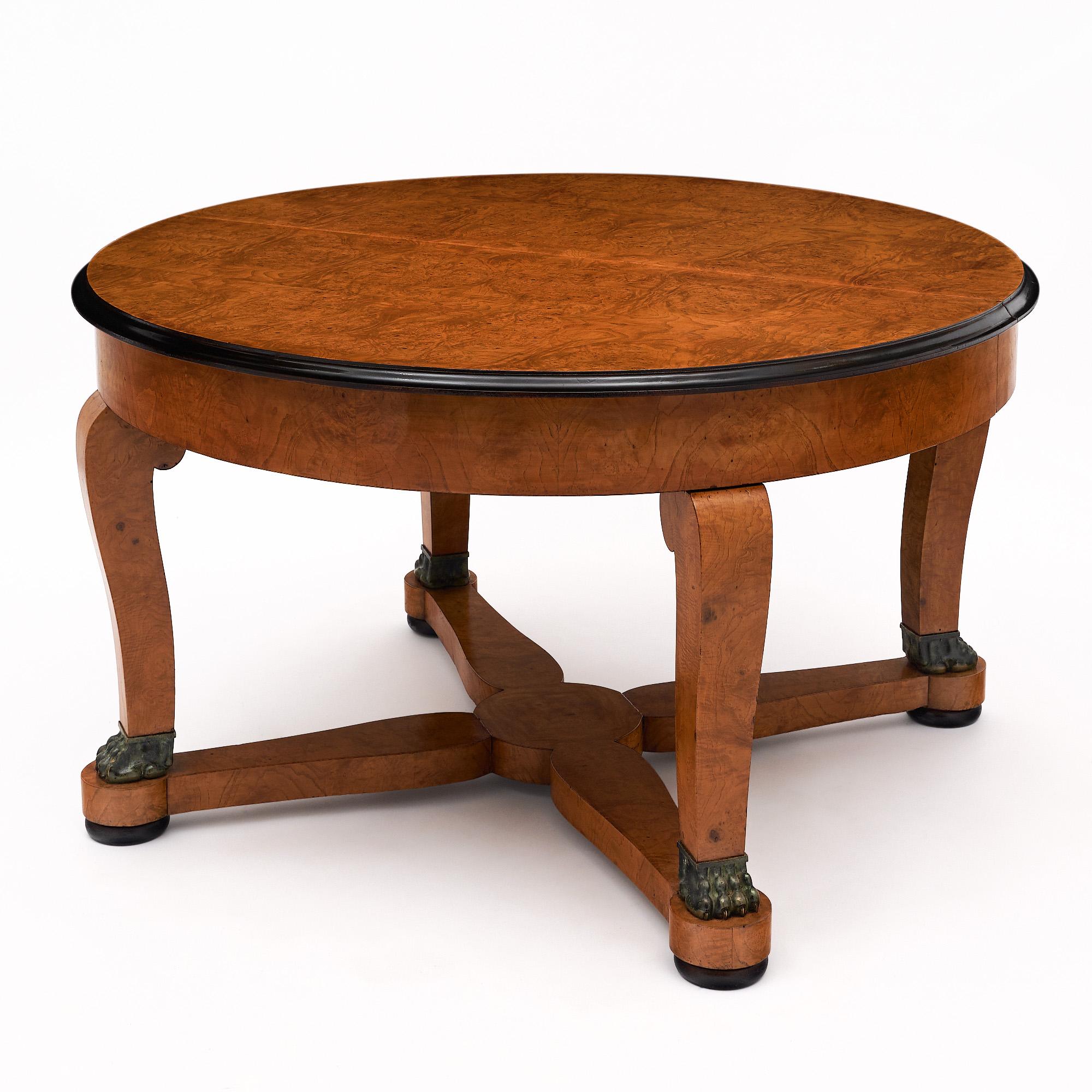 Library table in the French Empire style. This piece is made of solid ash and burled ash. Four curved legs are connected with an x-stretcher. Each leg boasts a bronze lion's paw foot. The table features ebonized detailing on the trim and feet. The