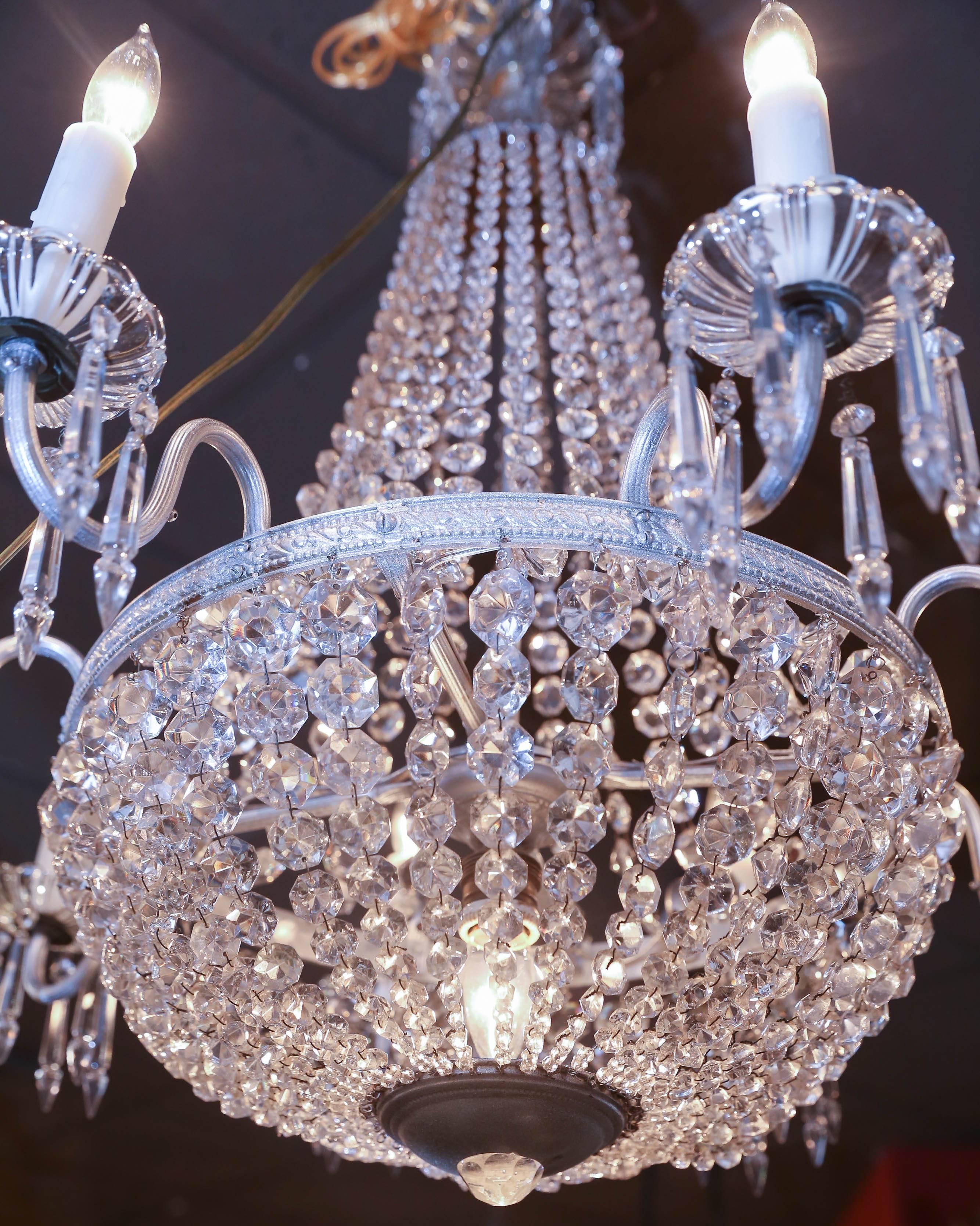 Silver tone metal sac-de-pearl empire chandelier with nine
lights, hung with clear crystal swags forming a drop dome,
canopy issuing eight scroll arms ending in crystal bobeches 
and faux candle fixtures, one fixture enclosed in drop