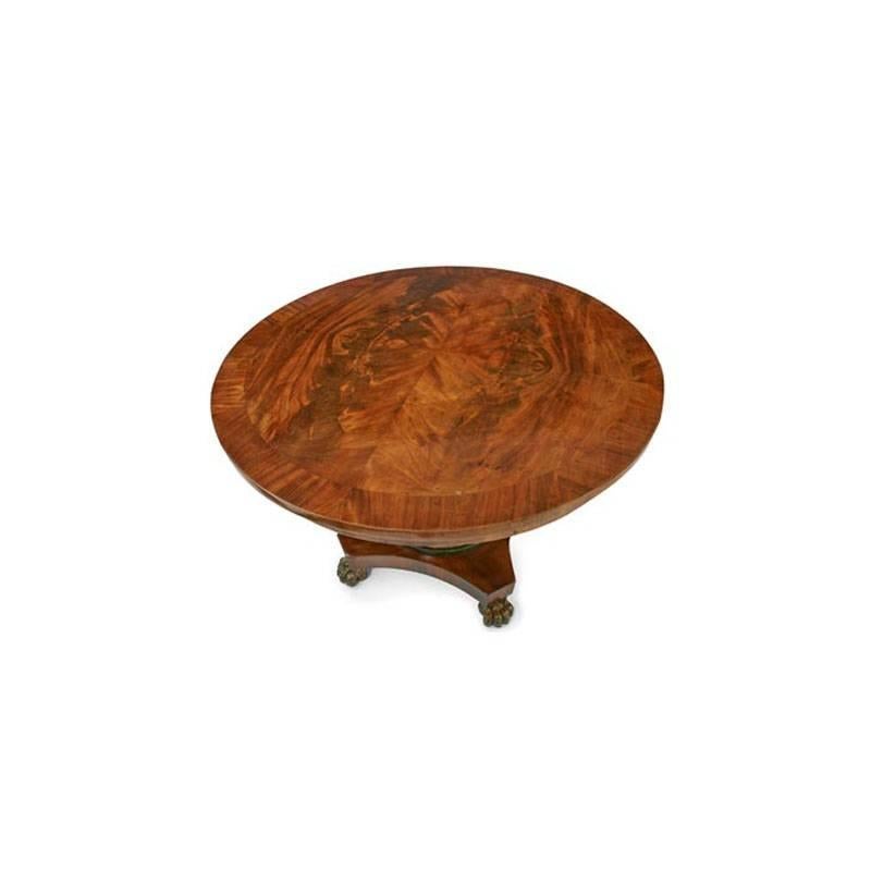 Mahogany veneered round tabletop with a mirrored pattern, a veneered skirt and vase shaped Stand in dark green with gilt details, on a stepped quatrefoil base with lion’s feet.
