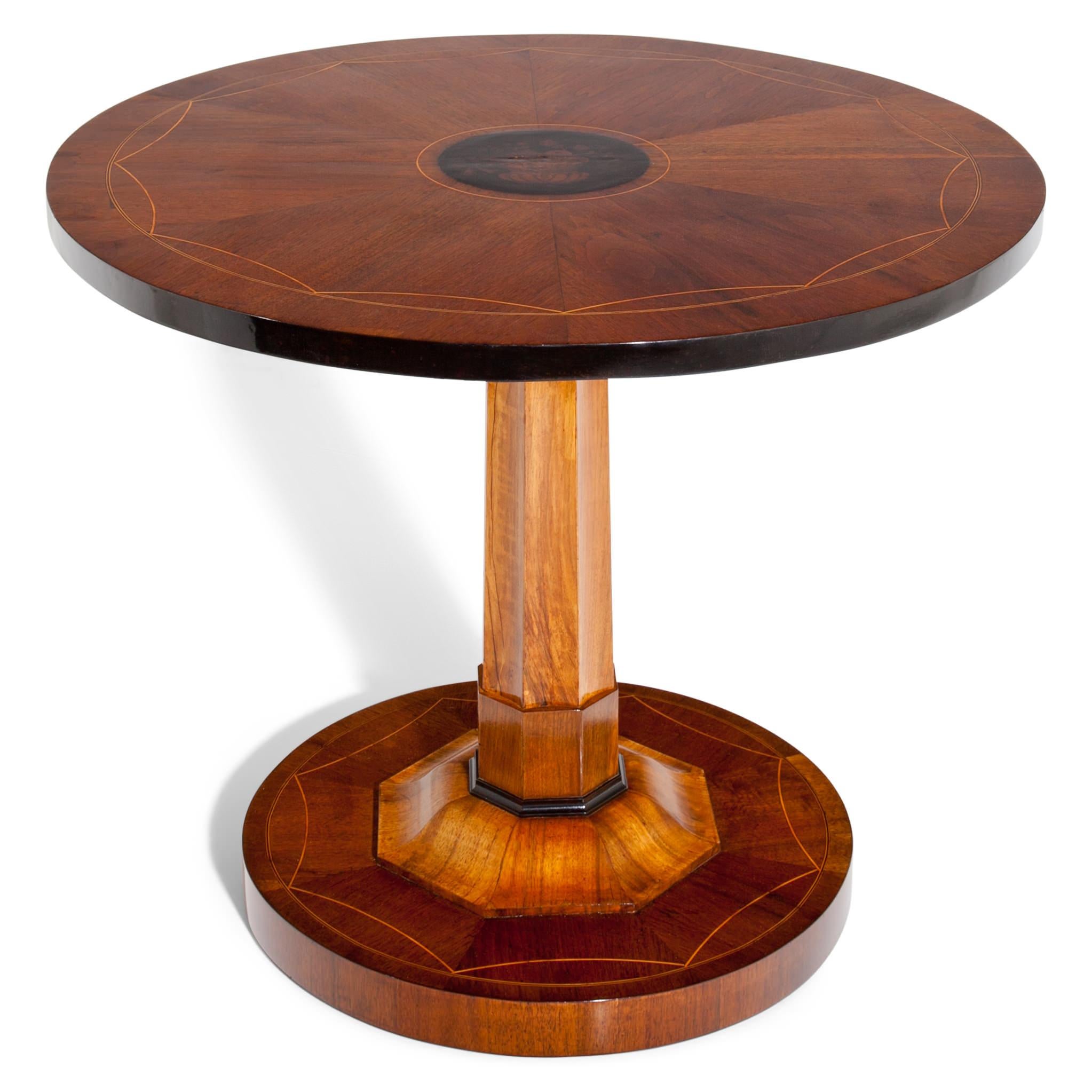 Empire salon table on a round base with an octagonal column and a round tabletop. The base and top are decorated with Fine thread inlays. The tabletop shows an Amphora with flowers, painted in ink. The tabletop folds down. The table is in a