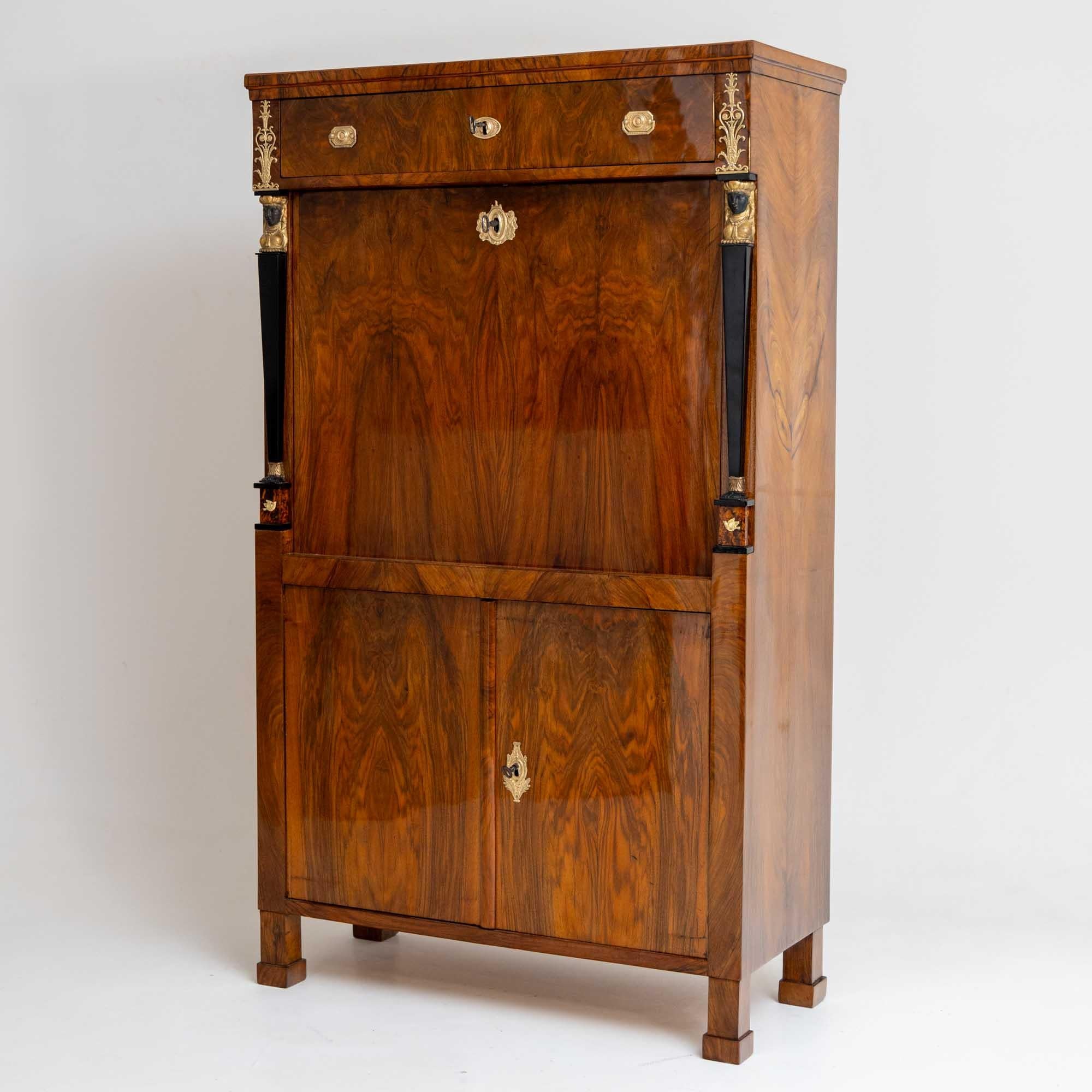 Empire secretary adorned with flanking caryatids around the flat writing flap, top drawer, and a two-door base cabinet. The caryatids are elegantly ebonized and gold-patinated, complemented by fire-gilt bronze fittings. The interior boasts several
