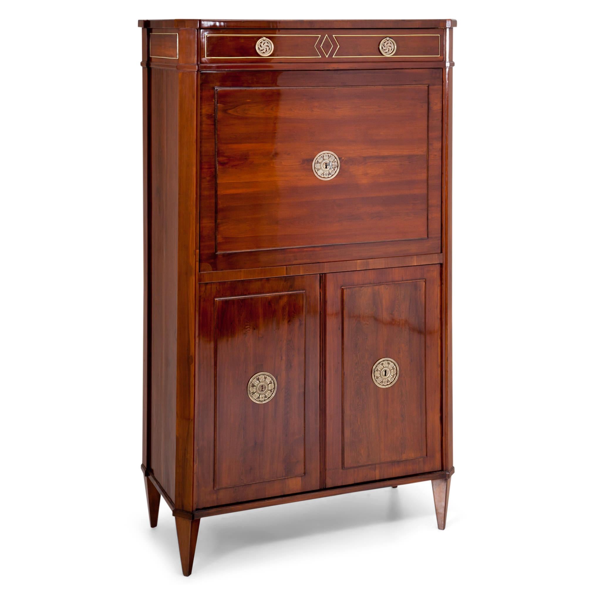 Viennese Empire secretaire out of yew-tree, with one top drawer and a two-doored base, standing on tapered feet. The body has slanted corners and fillings on the doors and writing surface. The secretaire is decorated with brass molding and rosettes.
