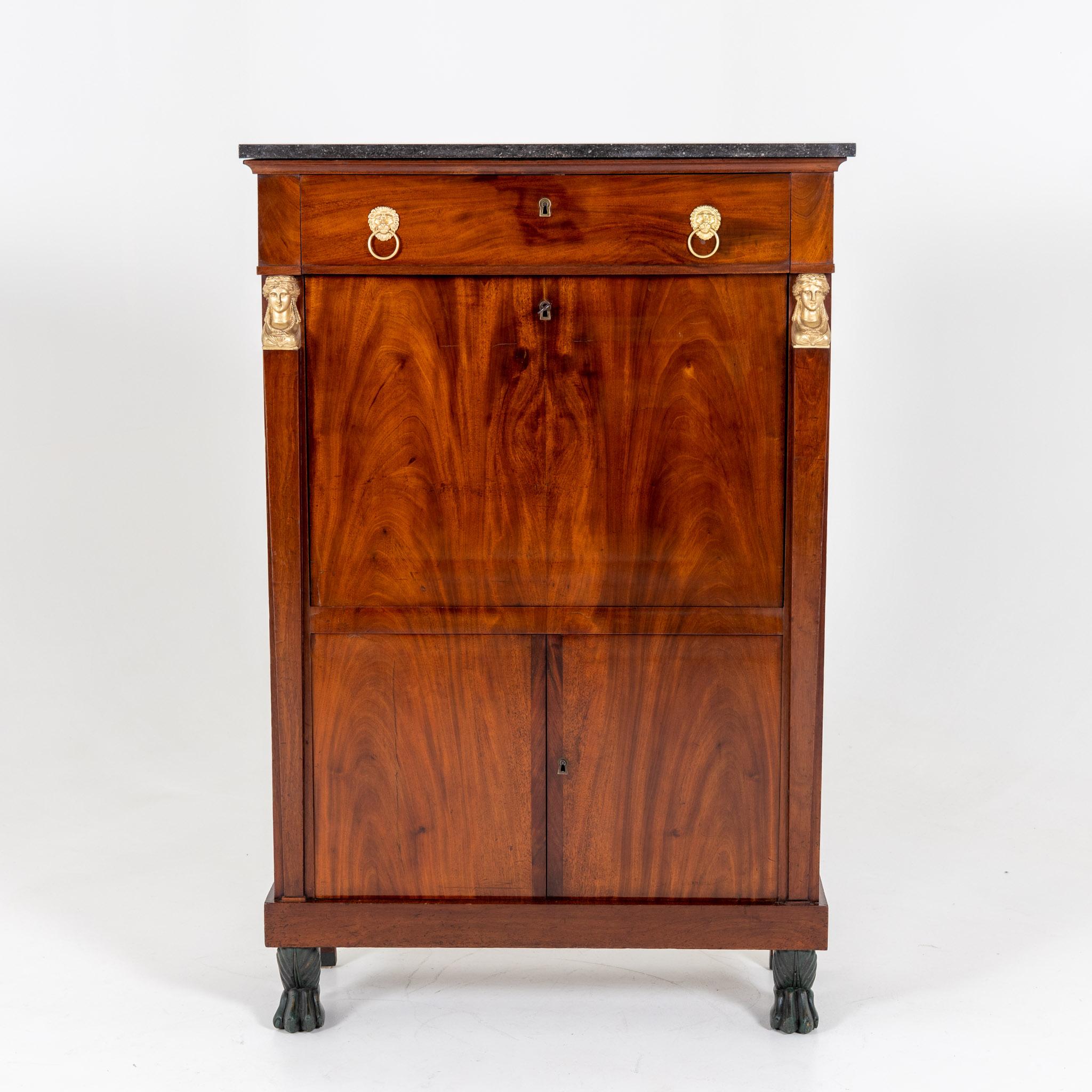 Secretary in mahogany veneer with two-door bottom part as well as dark marble shelf and fire-gilded fittings. Behind the writing flap with brown leather there are more drawers and compartments.