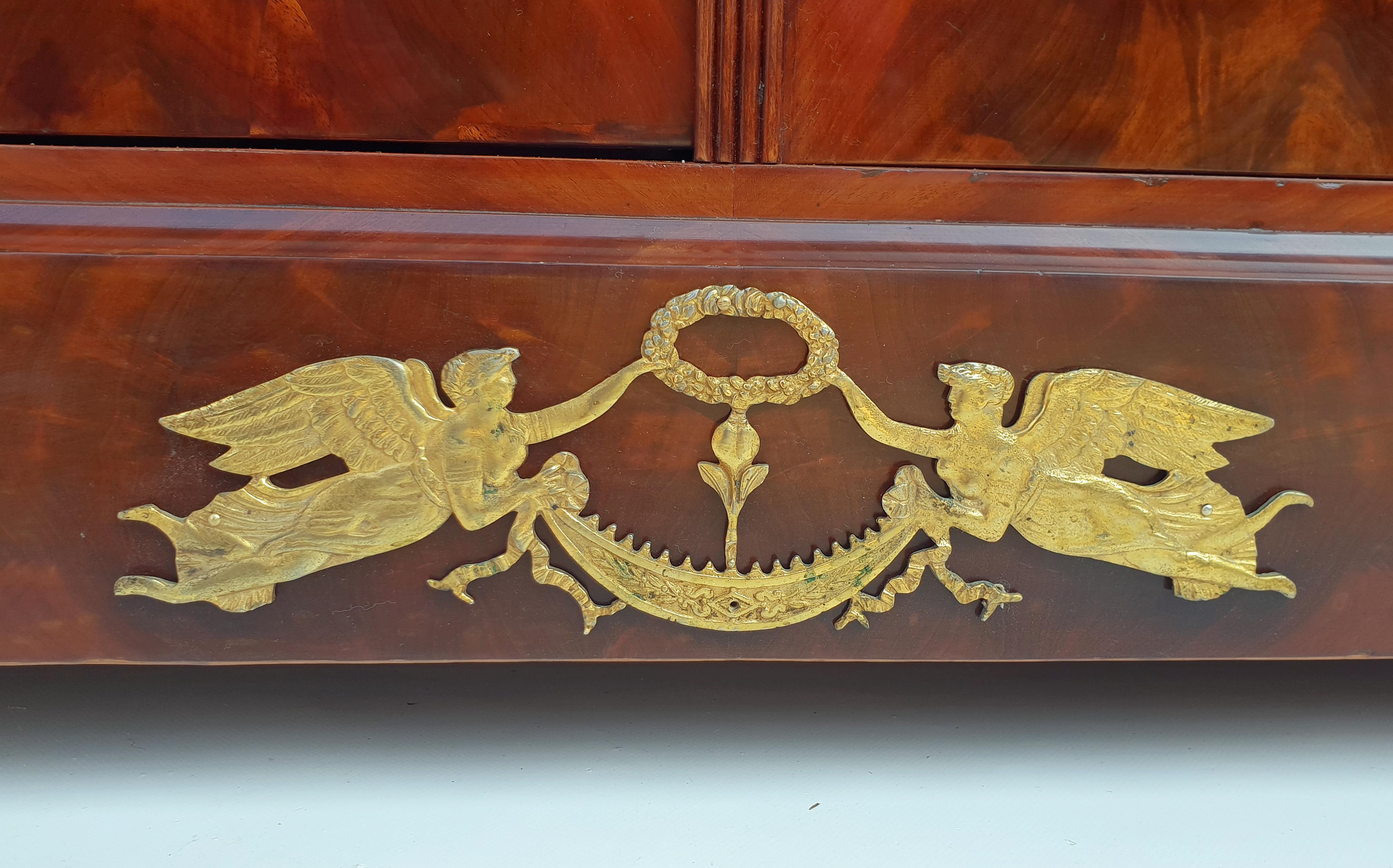 Empire sideboard, Paris, 1800s. Made of mahogany.

Wide pedestal with small bases and elaborate fire-gilt bronze with two angels holding a laurel wreath. Narrow pilaster strips, two doors in fine pyramid mahogany, original key plates and lock and