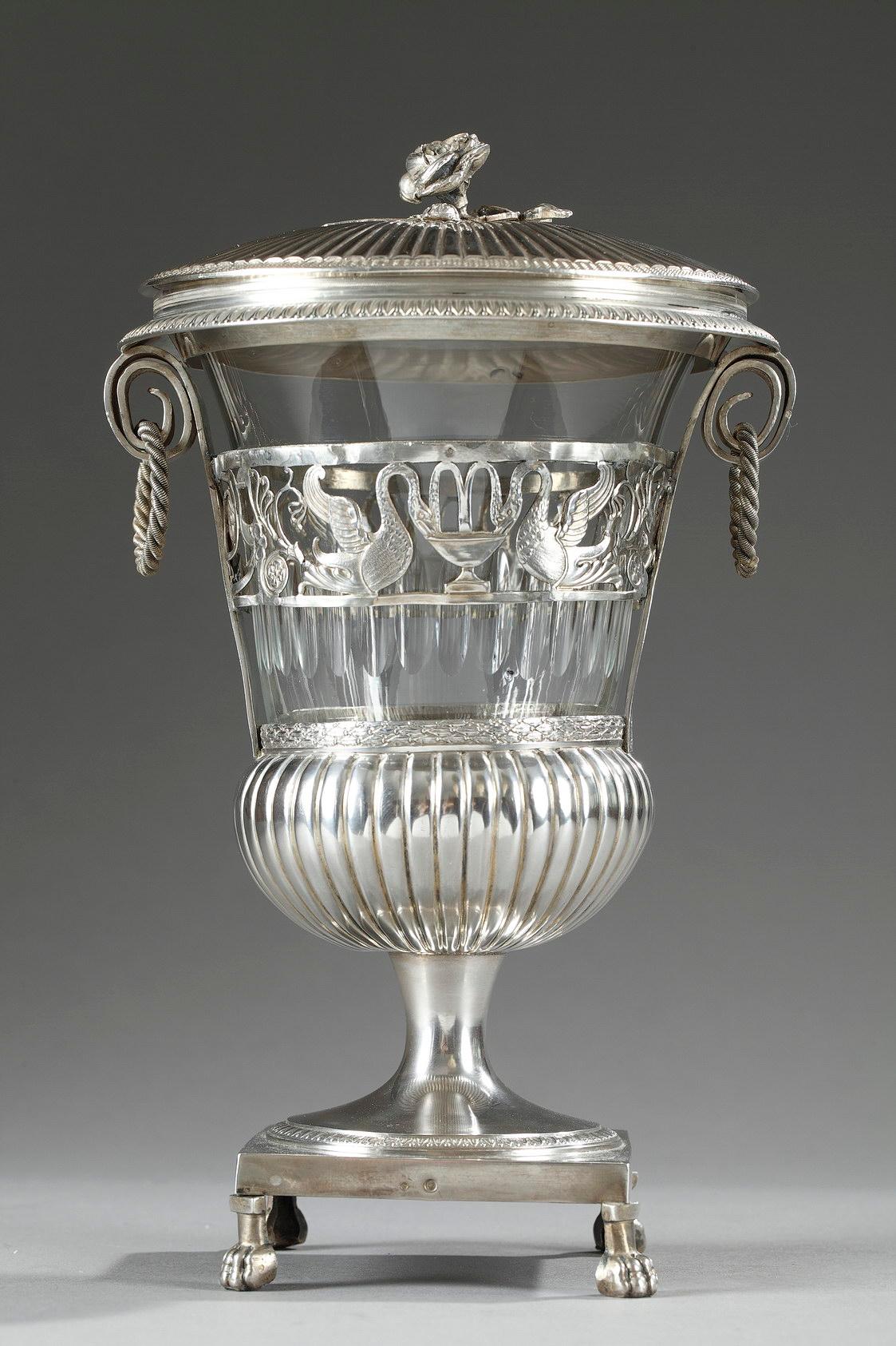 An early 19th century silver and crystal sweetmeat basket decorated with an openwork frieze depicting swans drinking from a fountain, rinceau and small flowers. Two rolled up stripes finely chiseled with branches form the handles, of which are