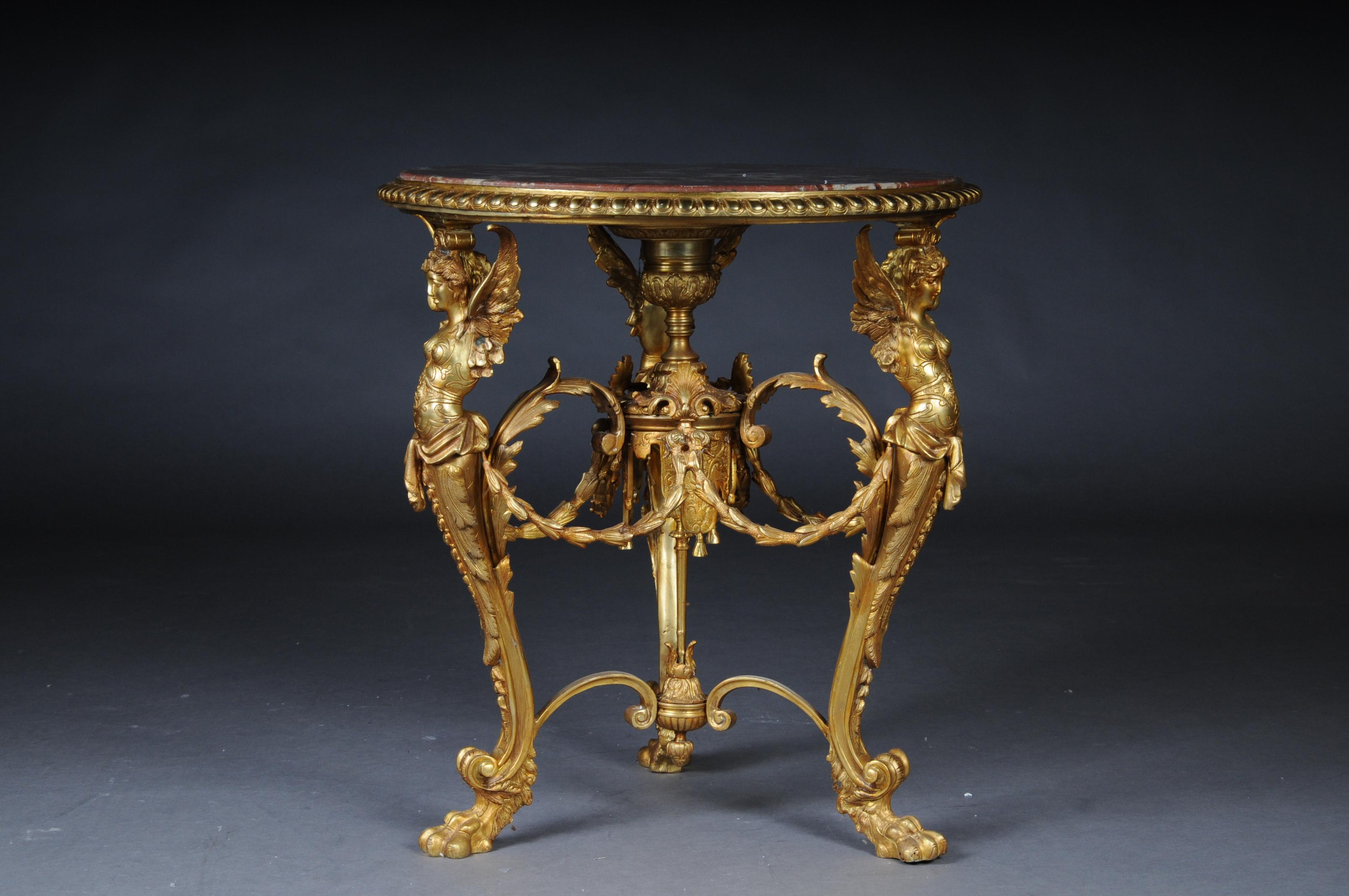 Finely chased and gilded bronze in wax casting. Three curly legs connected with gutter. Medium with garland-shaped decoration. The legs are in the form of three winged, fully plastic female bodies, ending in paw feet. Slightly protruding, round