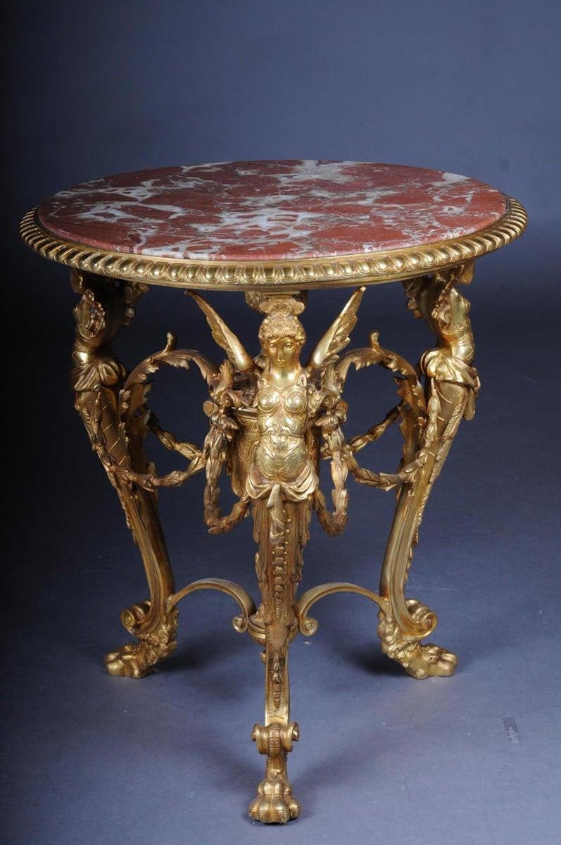 Bronzo finemente cesellato e dorato in fusione di cera. Tre gambe ricciolute collegate con una grondaia. Media con decorazione a forma di ghirlanda. Le gambe hanno la forma di tre corpi femminili alati, completamente in plastica, che terminano con