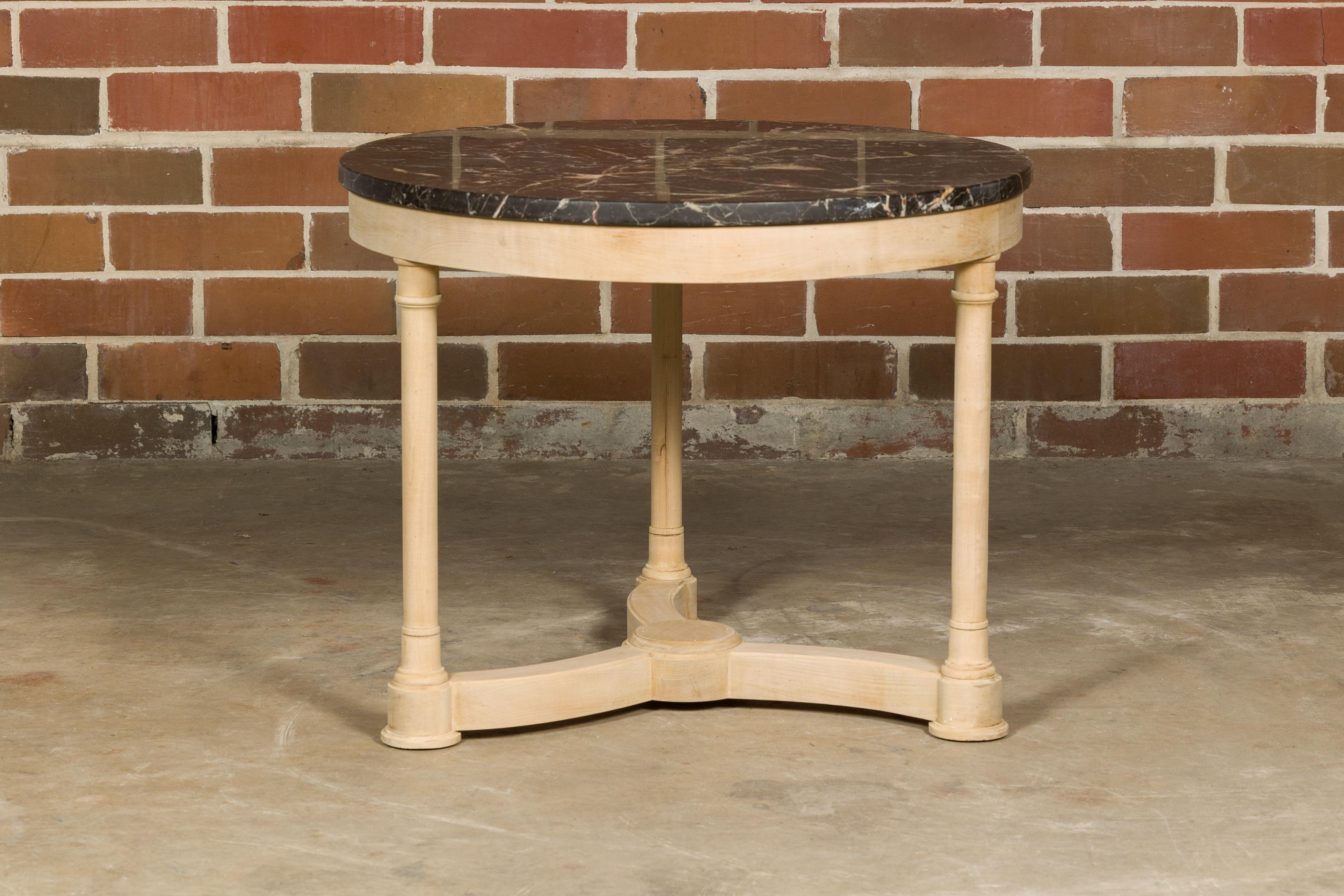 A French Empire style bleached walnut table from the 19th century with black veined circular marble top, three Doric column shaped legs and tripartite low stretcher. Evoke the grandeur of historical France with this immaculate 19th-century French