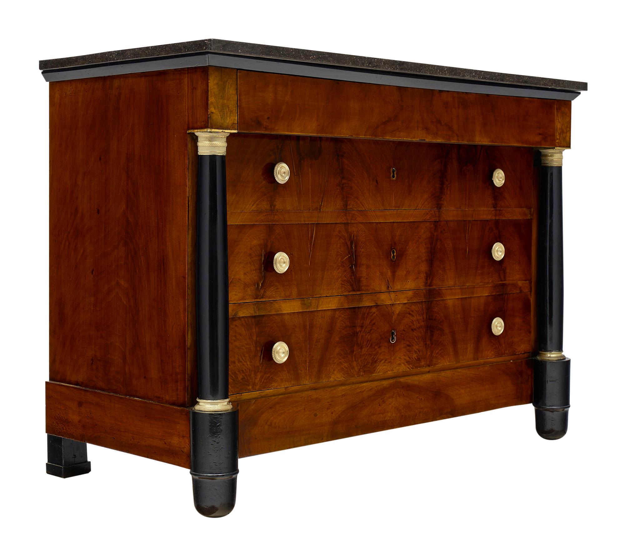Empire style antique French chest of drawers made of mahogany and finished with lustrous French polish. The detached columns are ebonized and feature finely cast gilt bronze hardware. We love the black marble slab which is original and intact. There