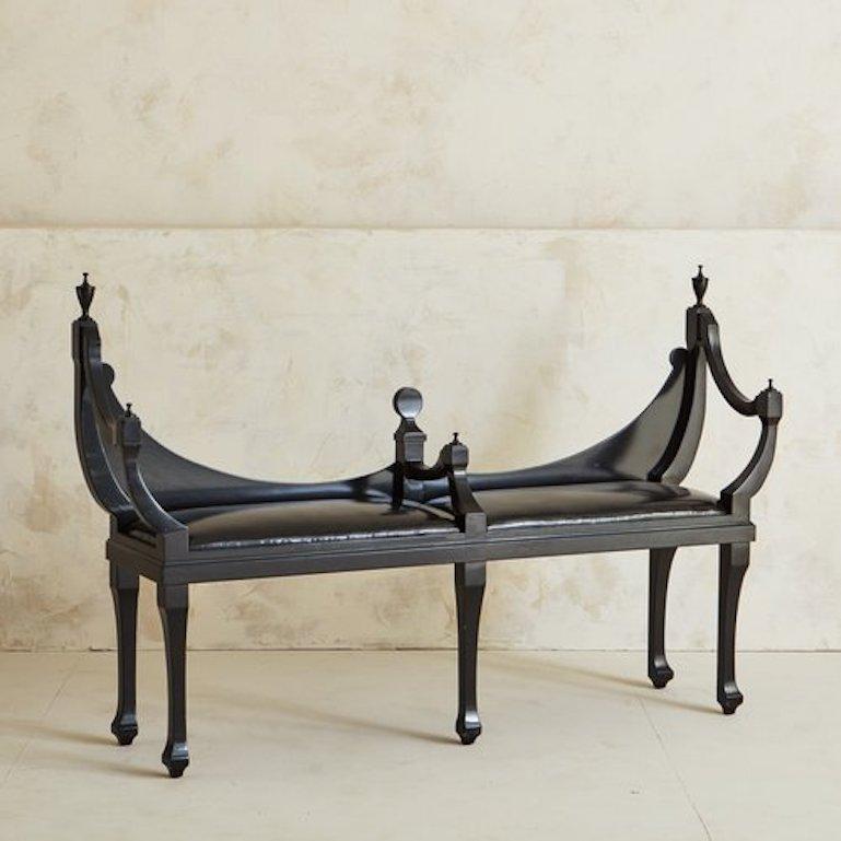 A stunning 1960s Empire style arched bench featuring an intricate, curved frame with decorative finial tops. The frame was constructed with wood and painted black. This bench has a black patent faux leather upholstered seat and five cabriole legs.