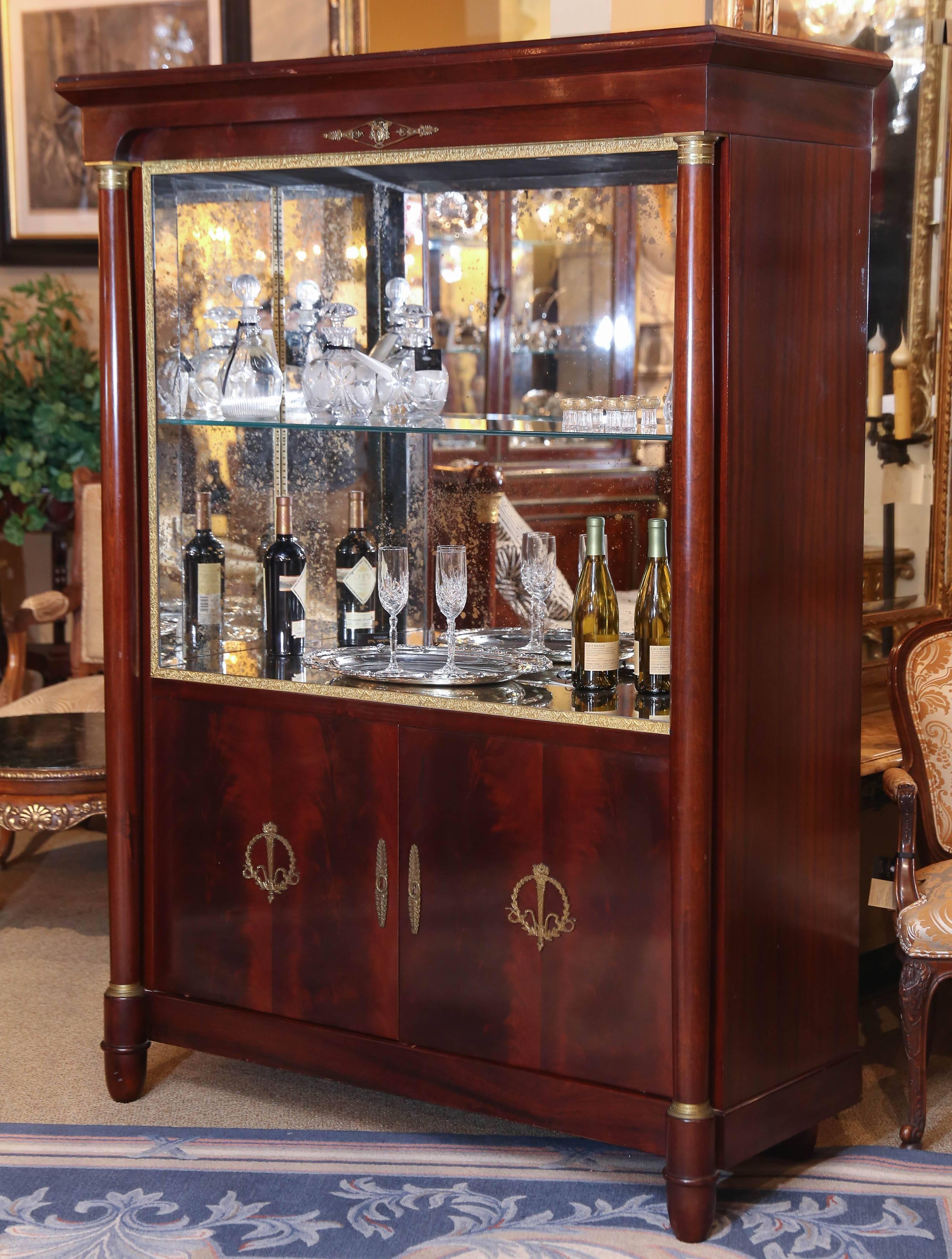 Impressive cabinet that can become a bar, bookcase or display
Made of mahogany and lined with antiqued glass with one
Moveable glass shelf. Bronze accents with a mask at the
Centre top and a wreath with a torch decorates the doors
of this