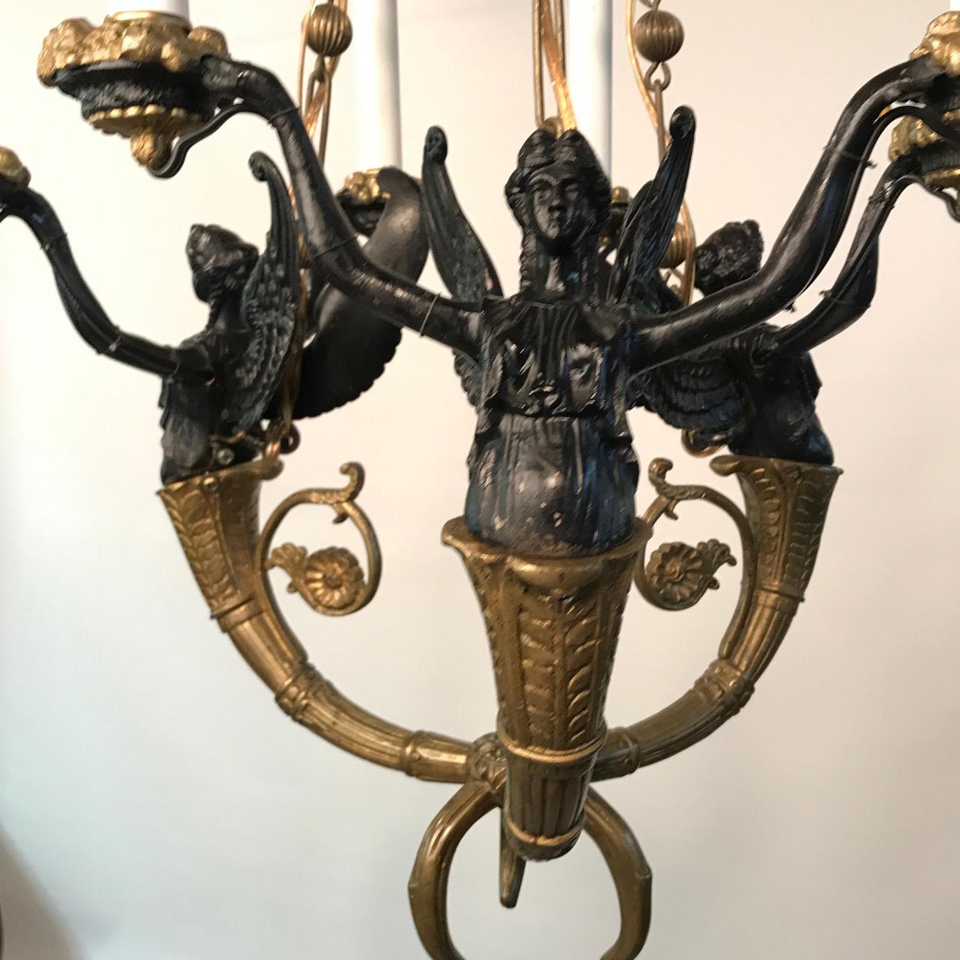 Antique French Empire style bronze six-light chandelier the arms modeled as stylized horns from which winged caryatids with outstretched arms support the candle sockets. The suspension chains alternate pierced oblong flat plates with lobed spherical