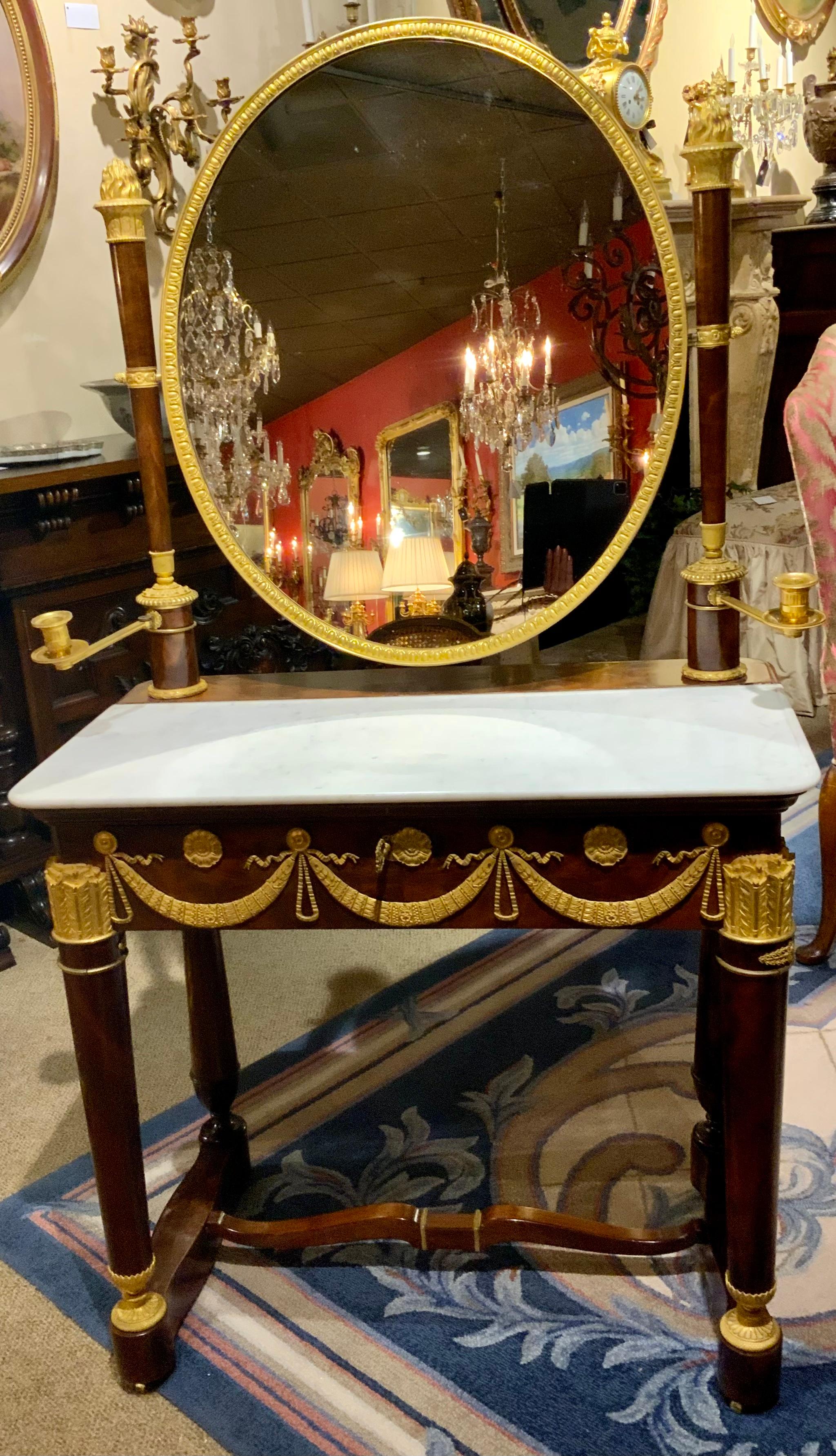 The circular mirror is encased in a bronze frame, supported by columns with 
A bronze dore flame capitals and swiveling candle arms, on a base with a
Dished white marble top over a swag mounted frieze drawer, raised on columns joined by an H form-