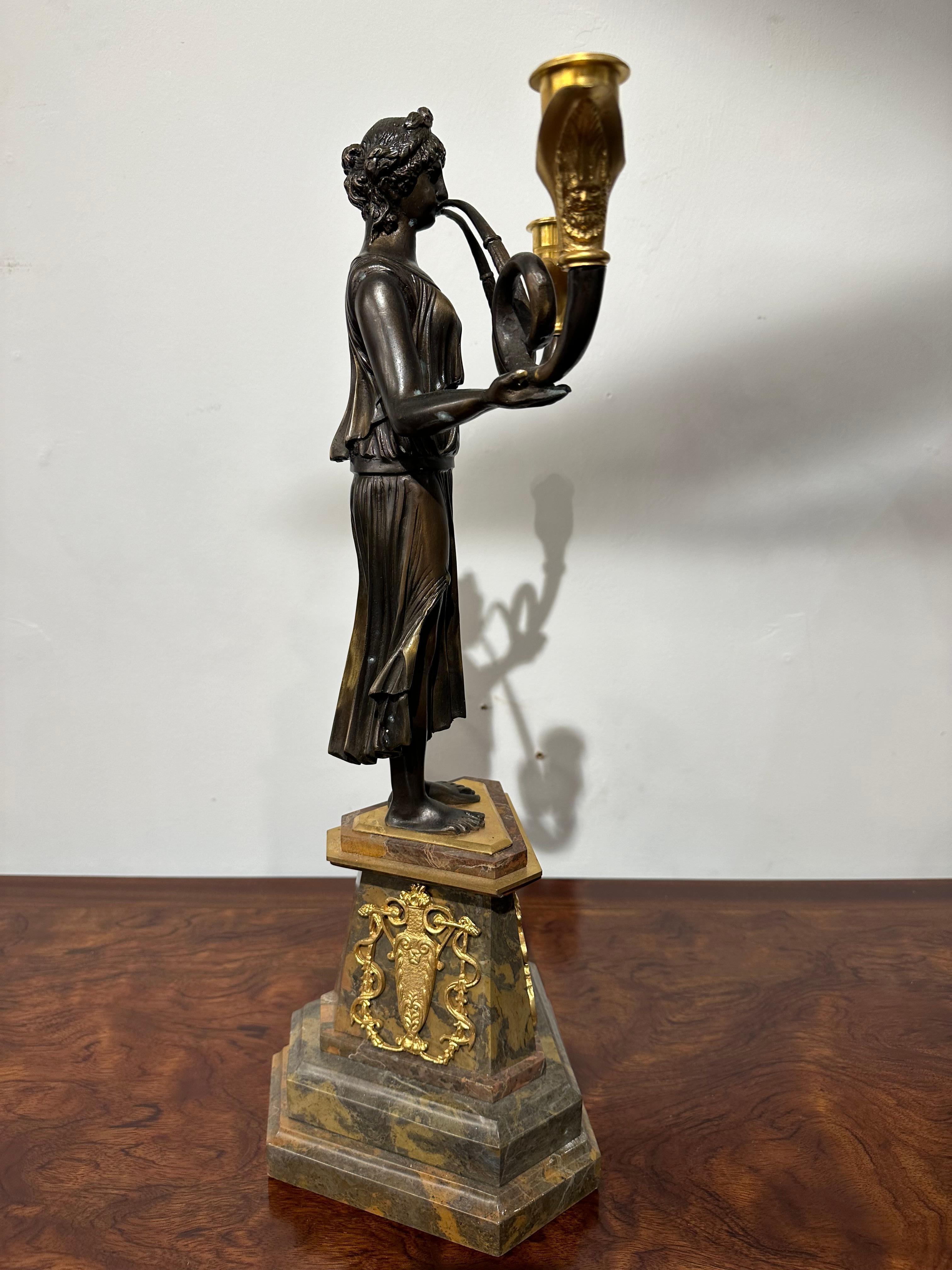 A beautifully made pair of French candelabras in bronze and marble. Two neoclassical styled women are blowing trumpet horns which form candlesticks. There is intricate detailing to their clothing and hair. Their faces are clearly depicted. A lovely