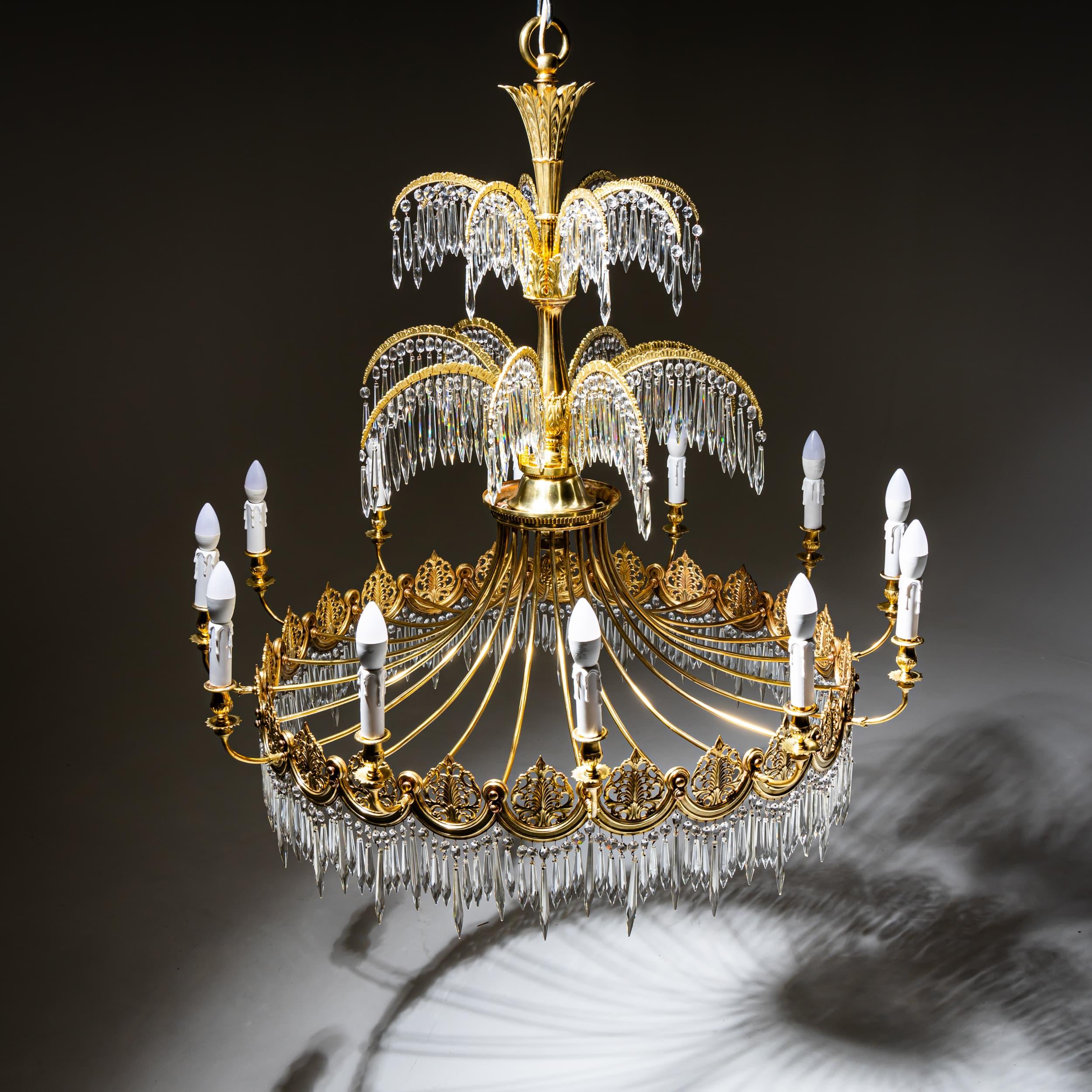 Impressive twelve-arm Empire-style chandelier featuring a scalloped ring adorned with finely detailed acanthus motifs and a rich arrangement of faceted glass prisms. The central shaft rises in two tiers above gently curved supports, decorated with