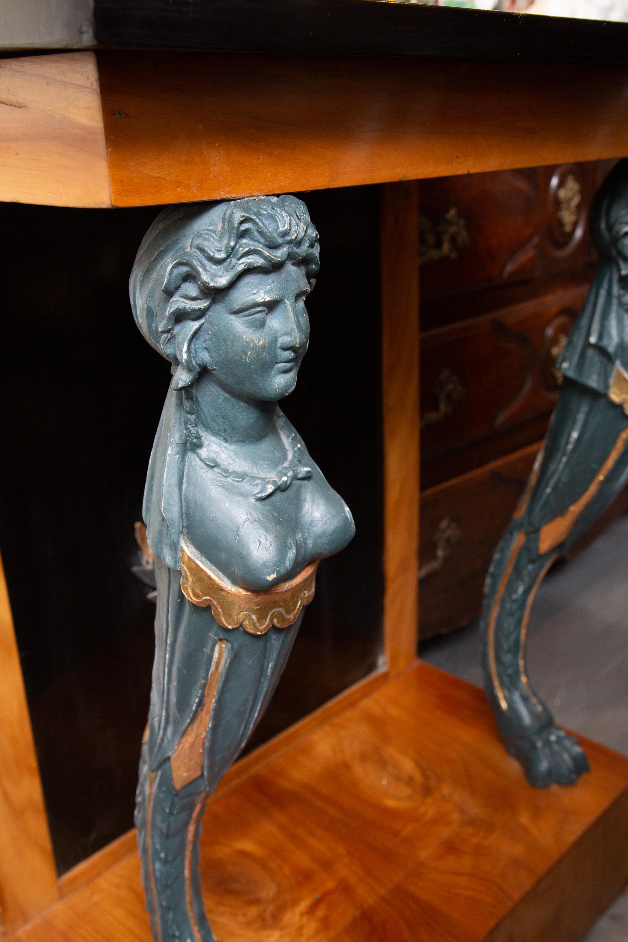 This is a very sophisticated Empire style console table, the ebonized plank top, over an ebonized wall centered with a carved parcel gilt laurel leaf supports depicting female forms ending in paw feet. The entirety of the console is situated on a