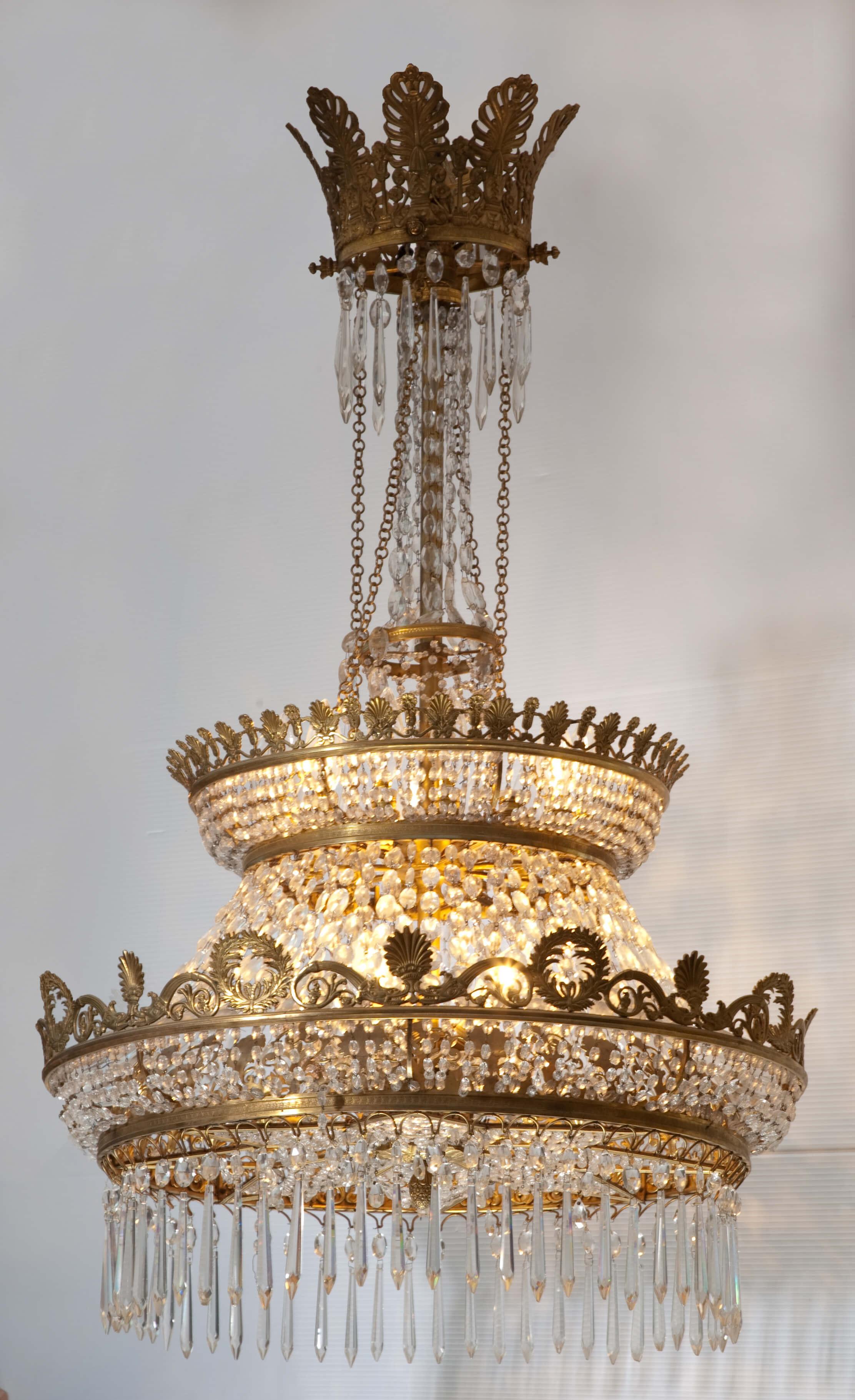 An Empire style chandelier in gilded bronze and cut crystal. The large central ring is embellished with palmettes and wreaths and supports beaded chains and long crystal French drops. The underside of the ring is star shaped and woven with crystal
