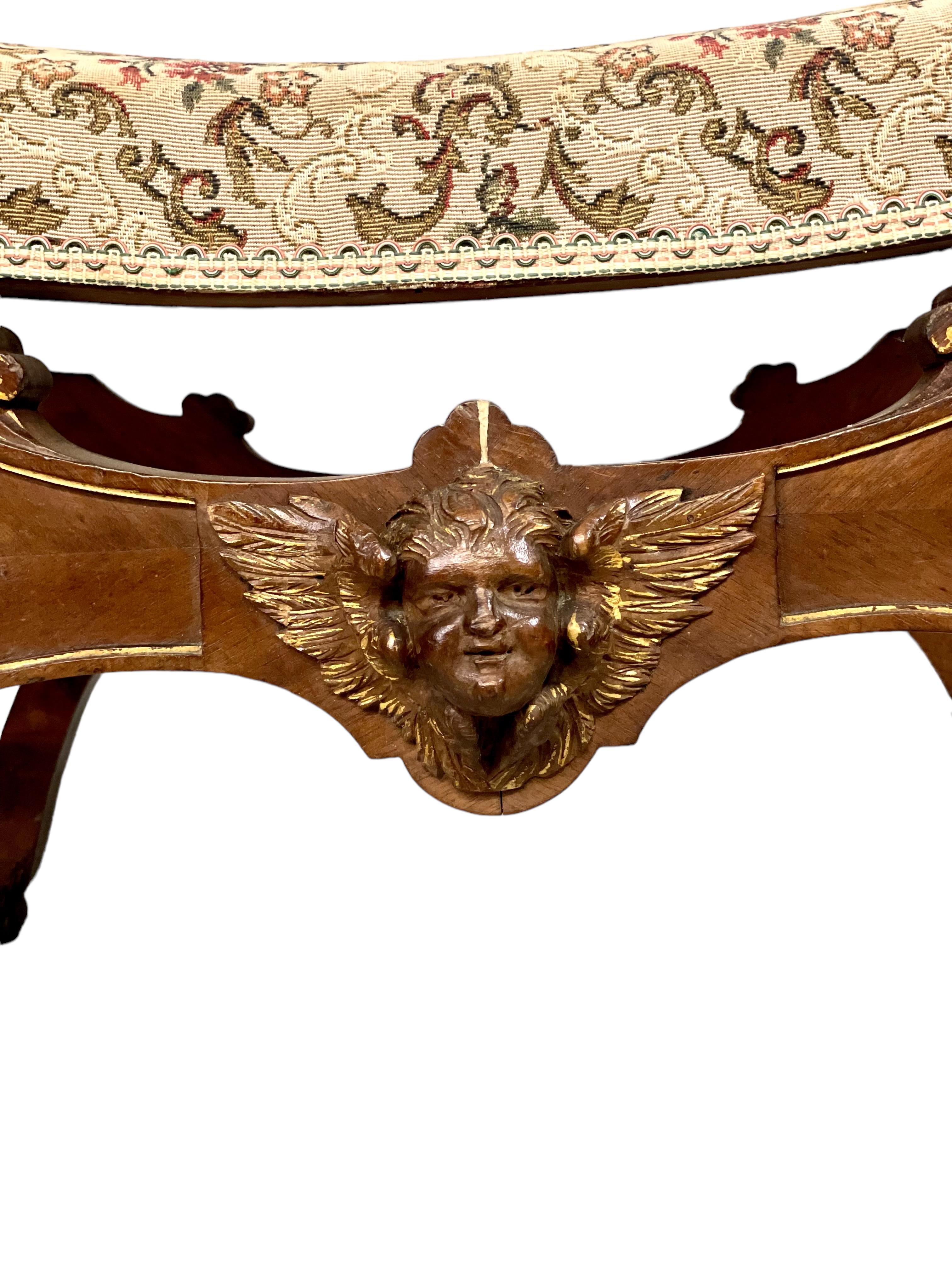 Elegantísimo taburete de curules de estilo Imperio del siglo XIX, sobre patas en X curvadas y chapadas, unidas por un bastidor torneado en forma de balaustre y rematadas en patas de león. El asiento acolchado está tapizado en brocado de color neutro