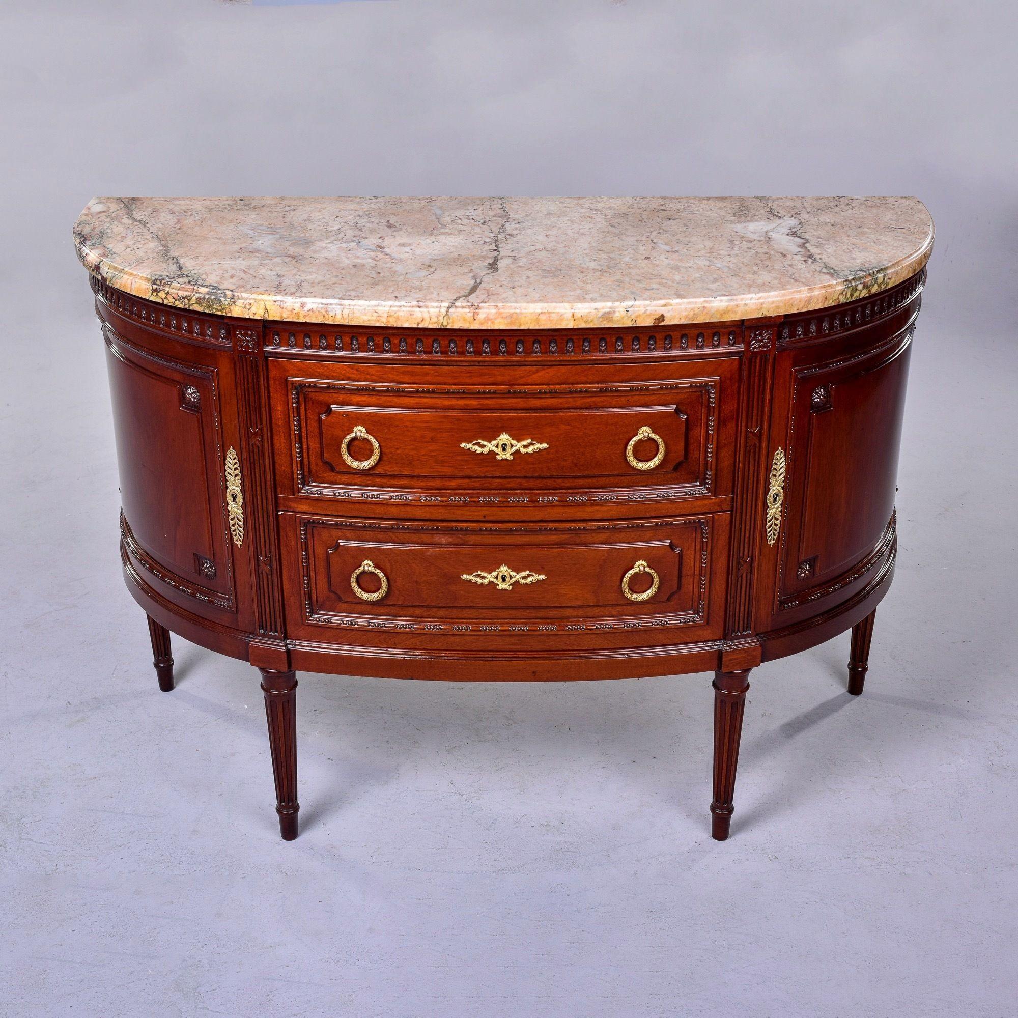 Found in France, this circa 1910 empire style demi lune commode is made of mahogany with a marble top. Commode has two locking drawers flanked by wedge-shaped, locking side cabinets. Four reeded and tapered legs, decorative carved details, brass