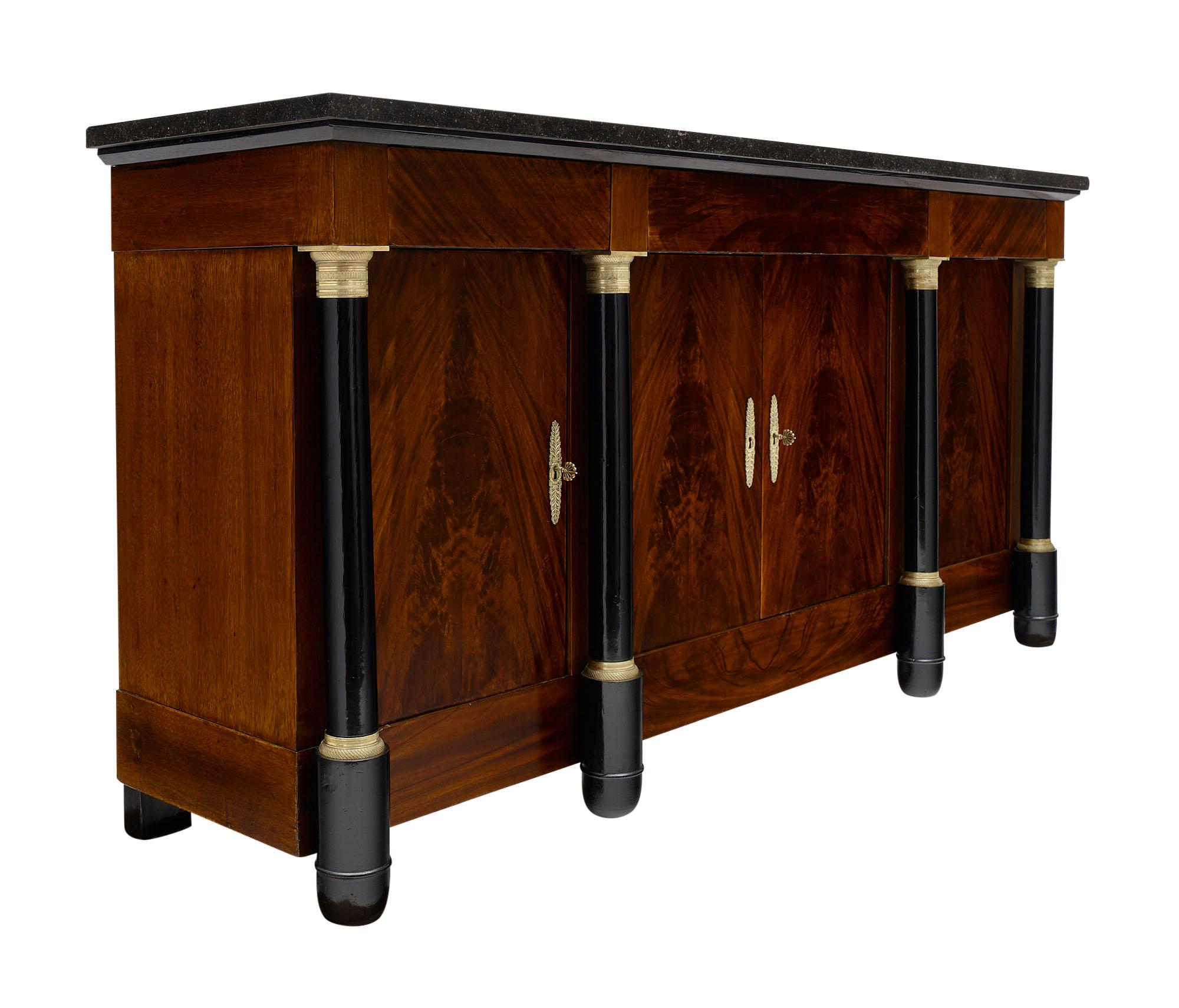 Empire style French antique buffet made of Cuban flamed mahogany finished in a lustrous Museum quality French polish. The columns are ebonized and feature finely cast gilt bronze hardware. The doors open to interior shelving and are topped by three